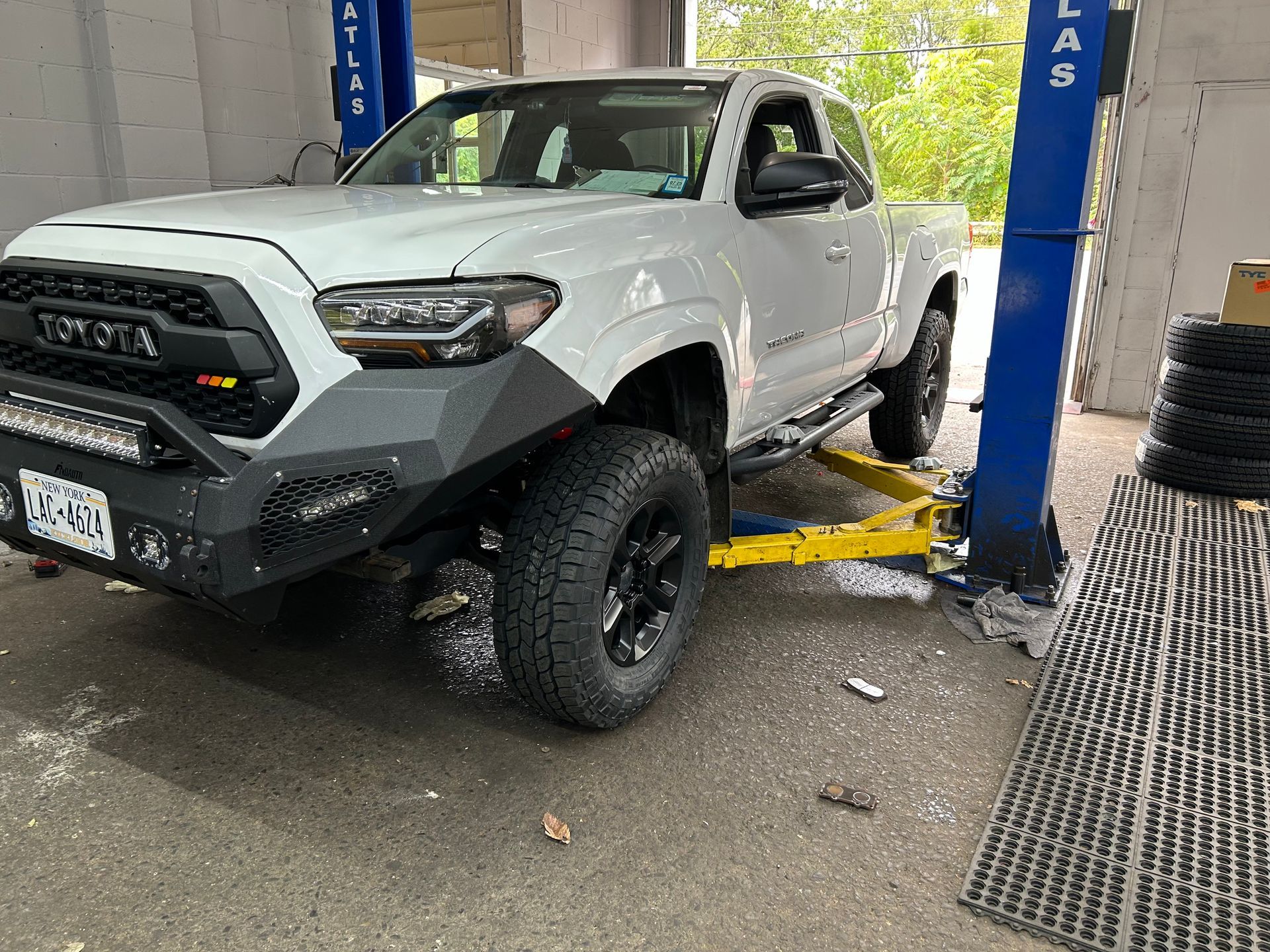 A white toyota tacoma is parked on a lift in a garage.