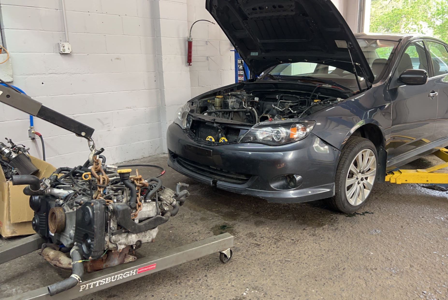 A car with its hood up is being worked on in a garage.