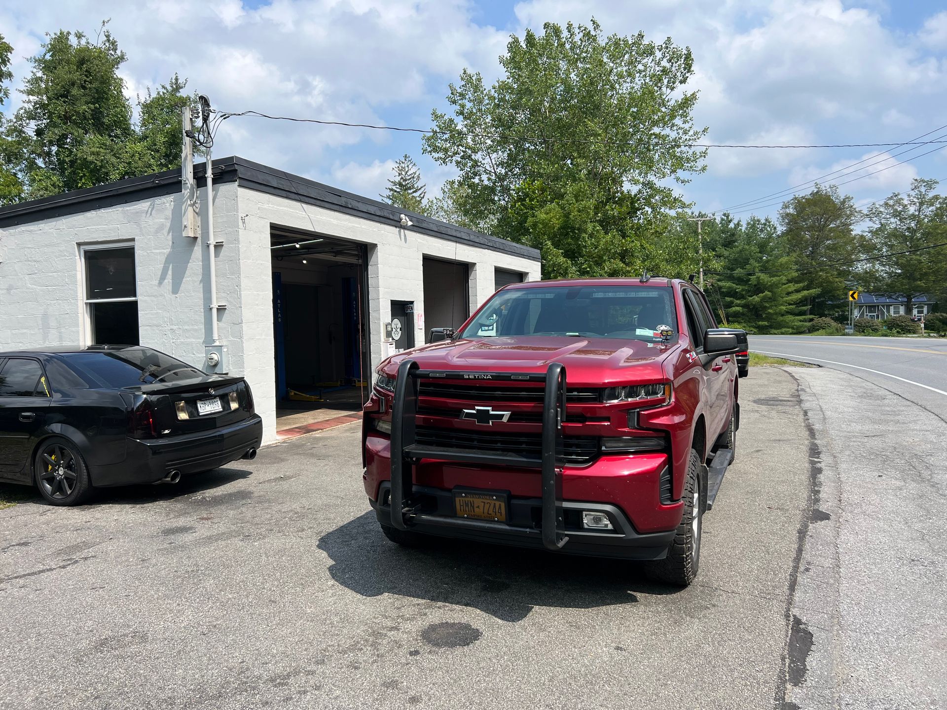 A red truck is parked on the side of the road in front of a garage.