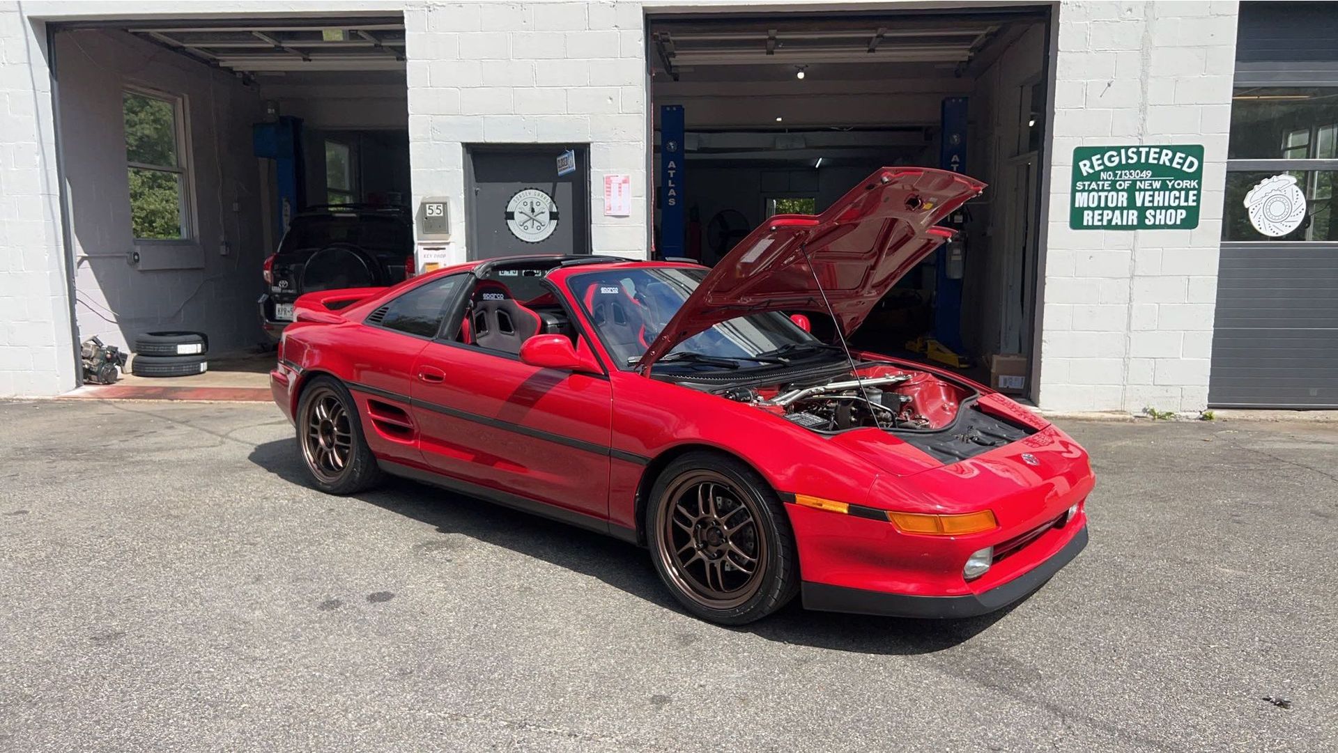 A red sports car with the hood up is parked in front of a garage.