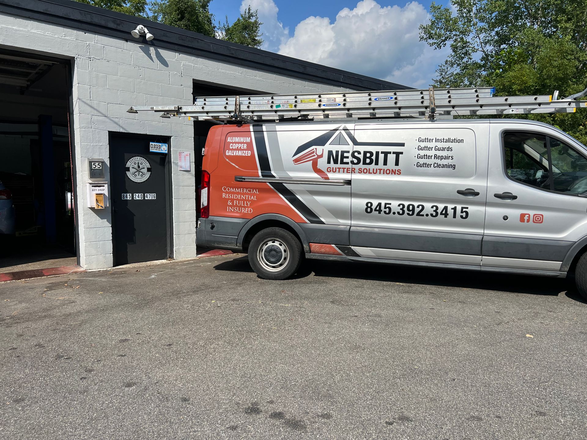 A van with a ladder on top of it is parked in front of a building.