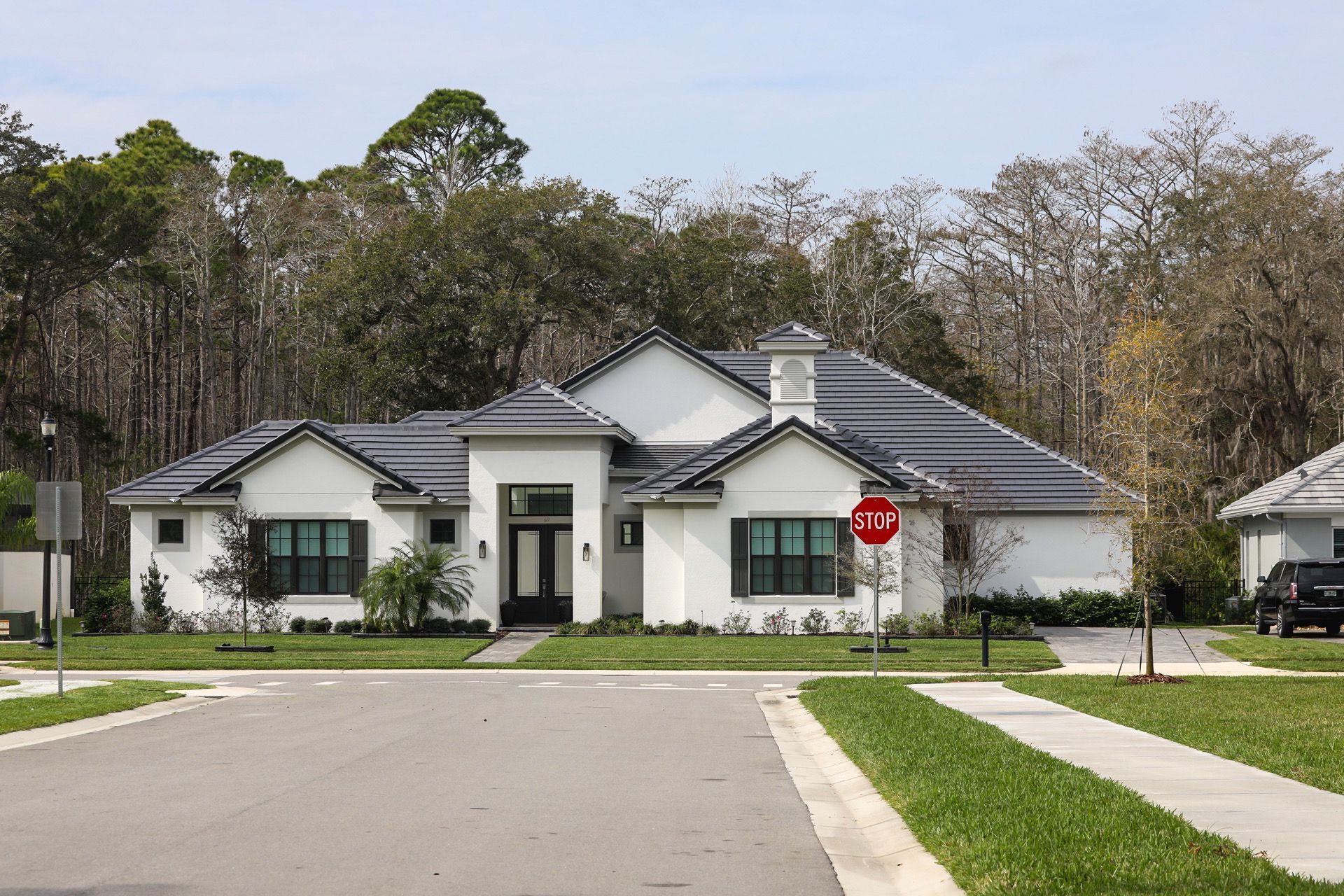 Suburban house with gray roof, white exterior, and a stop sign at the end of a quiet street