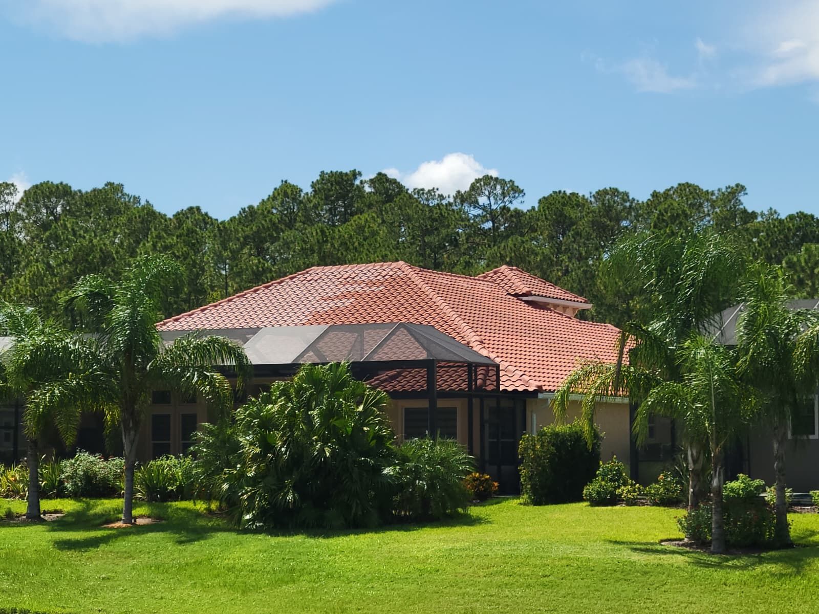 Single-story house with a red tile roof and screened patio, surrounded by lush green lawn and trees.