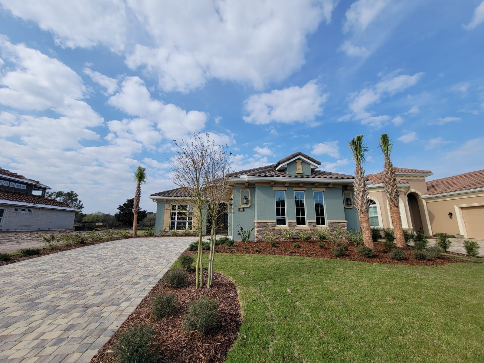 Single-story house with a stone driveway, green lawn, and blue sky with clouds