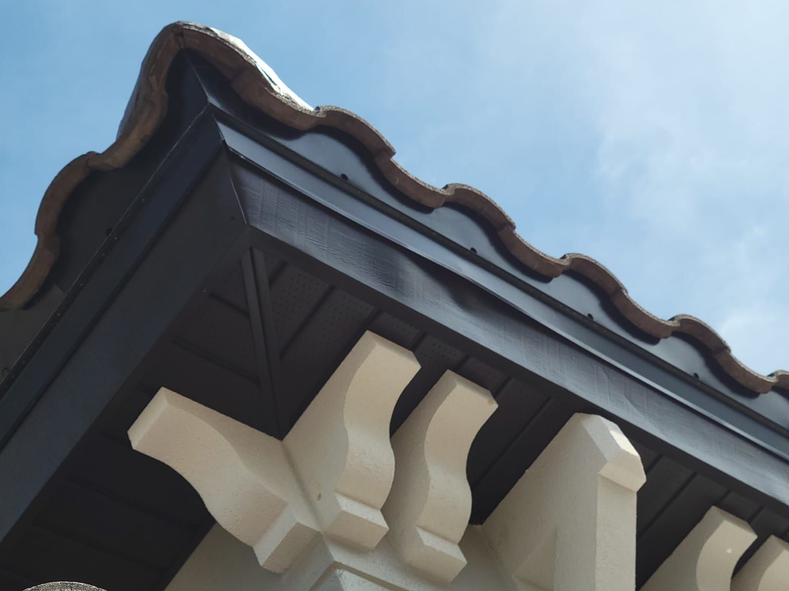 Close-up of a building eave with dark trim, white brackets, and a blue sky background