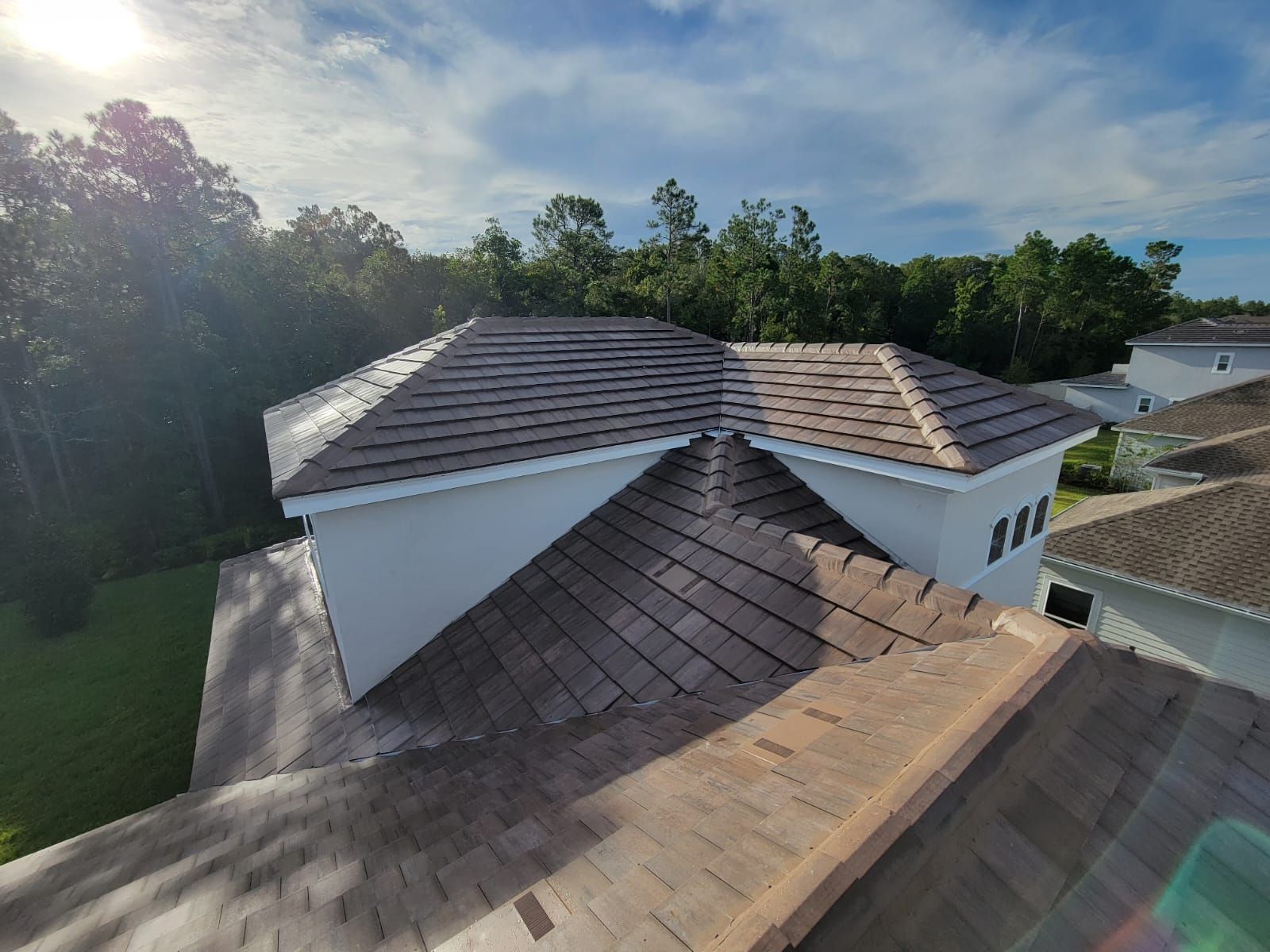 Aerial view of a house with a brown shingle roof beside trees under a cloudy sky