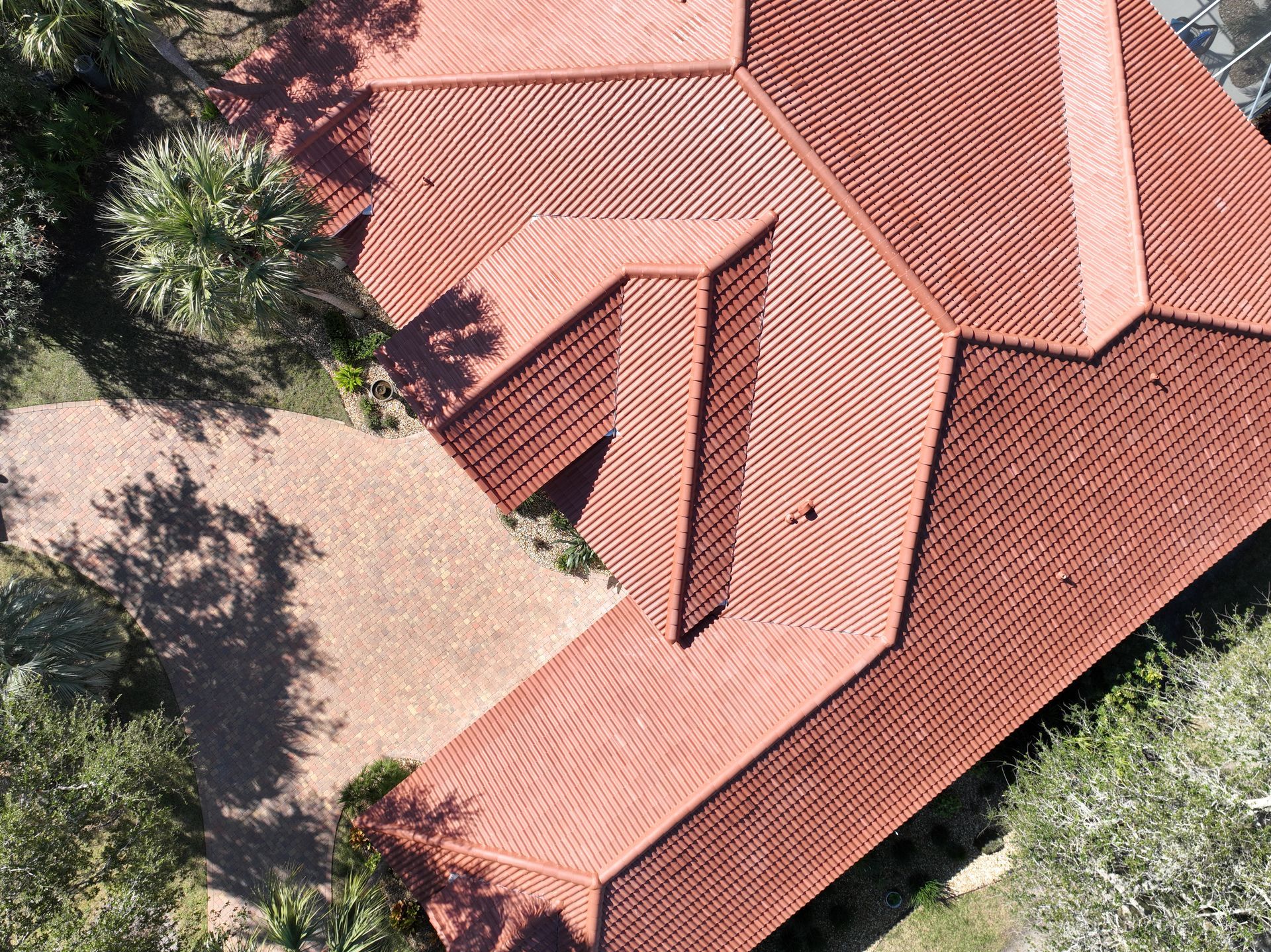 Aerial view of a red-tiled roof surrounded by trees and a paved courtyard