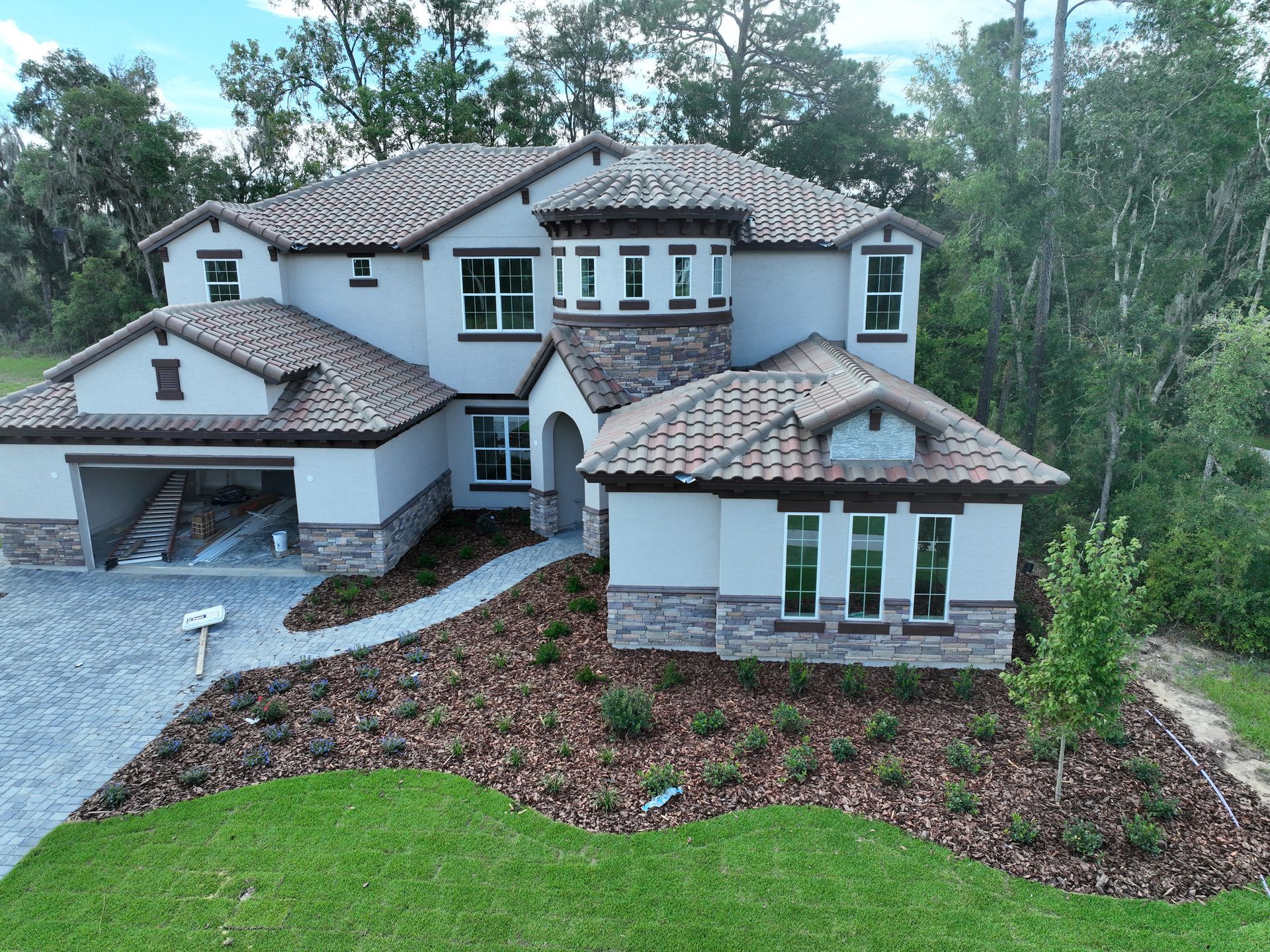 Large two-story white house with gray roof, front garage, and landscaped yard by trees