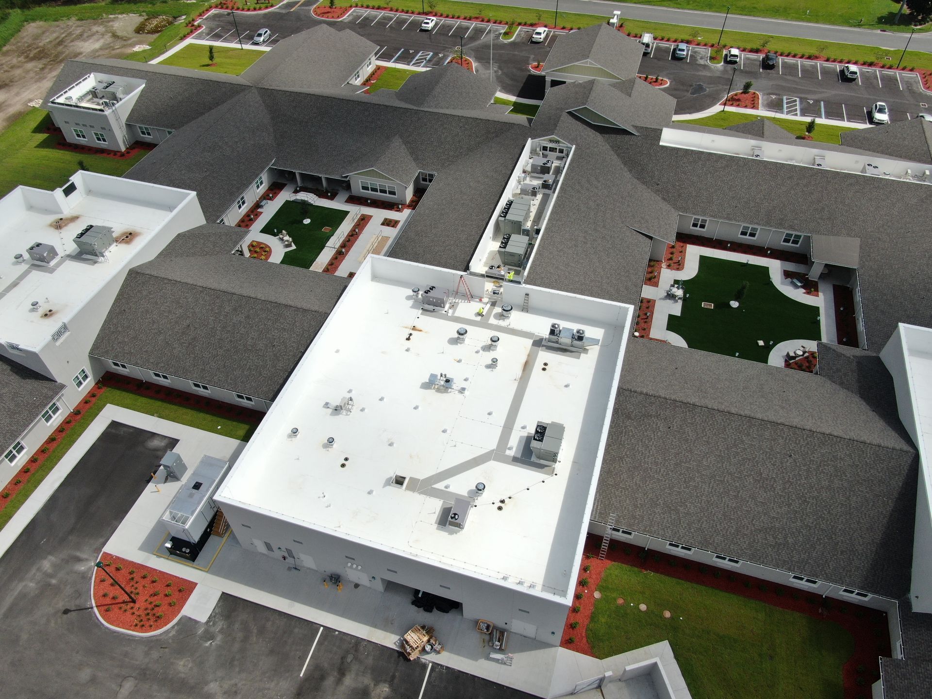 Aerial view of a modern building complex with white and gray roofs, courtyards, and landscaped areas