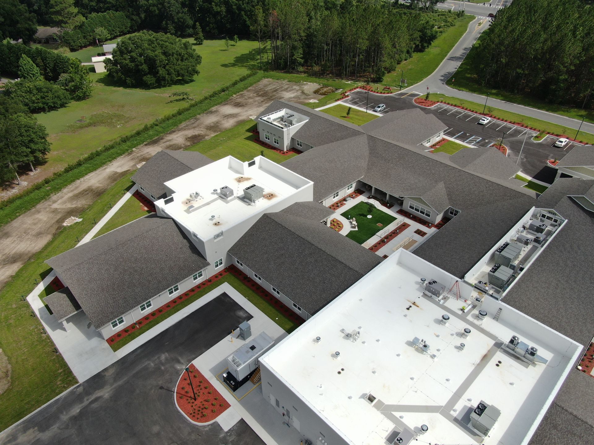 Aerial view of a modern building complex with white roofs, courtyards, and surrounding greenery.