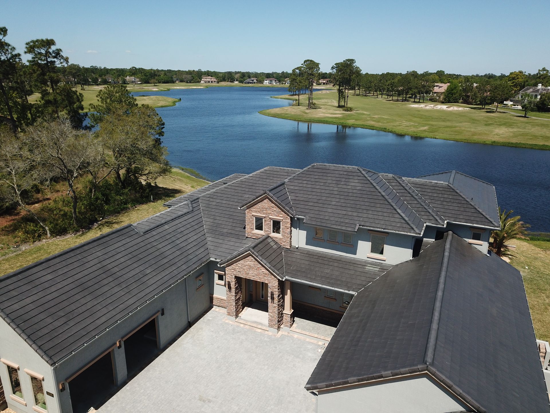 Aerial view of a large gray house beside a blue lake and green golf course.