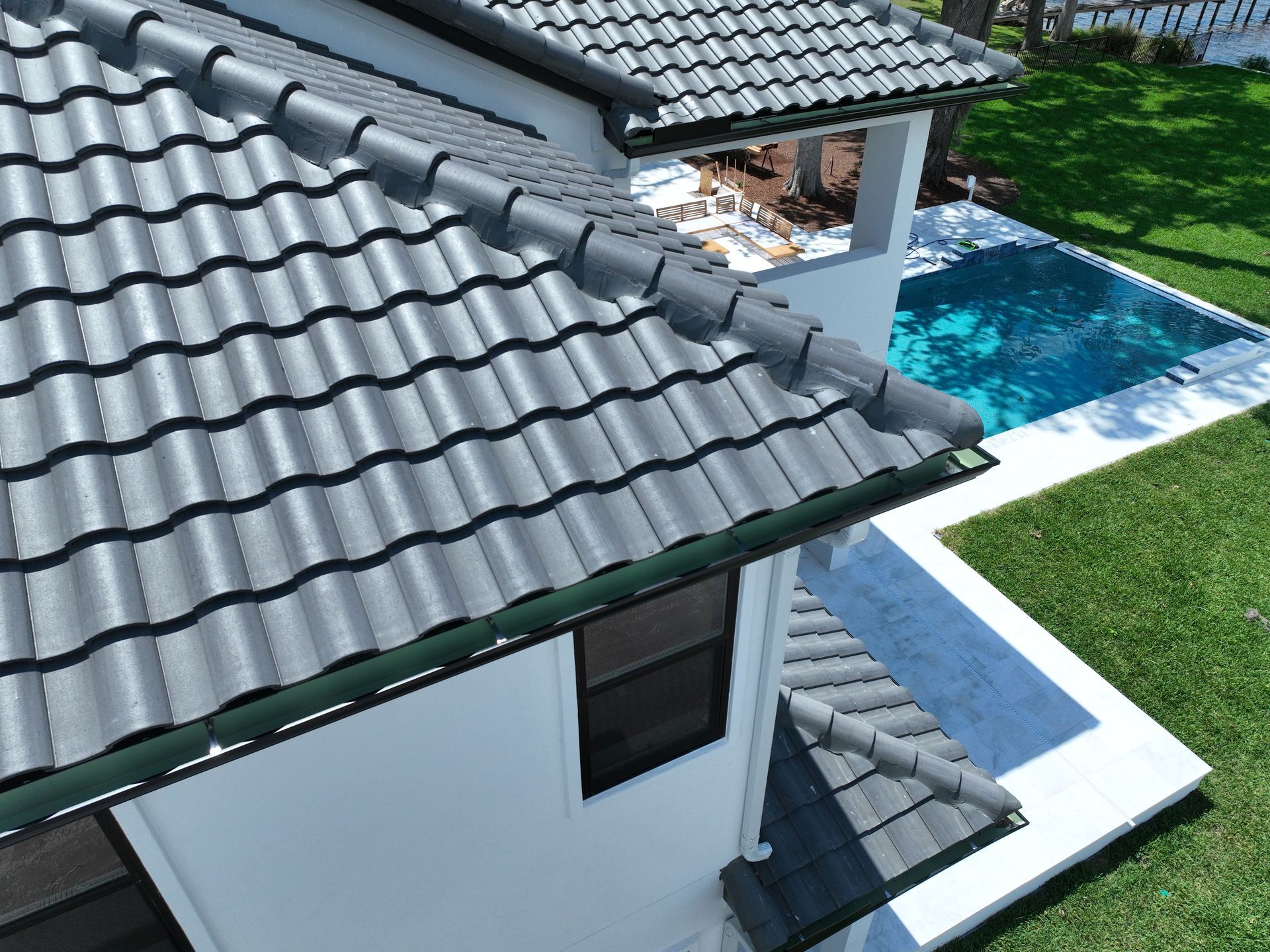 Modern house with dark tile roof beside a blue backyard pool and patio