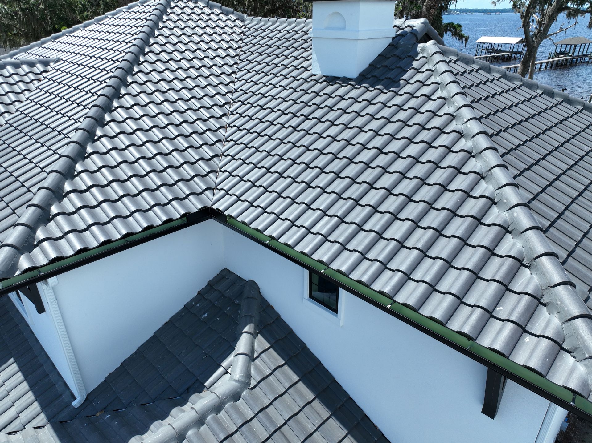 White house roof with gray tiles and a chimney, viewed from above on a sunny day