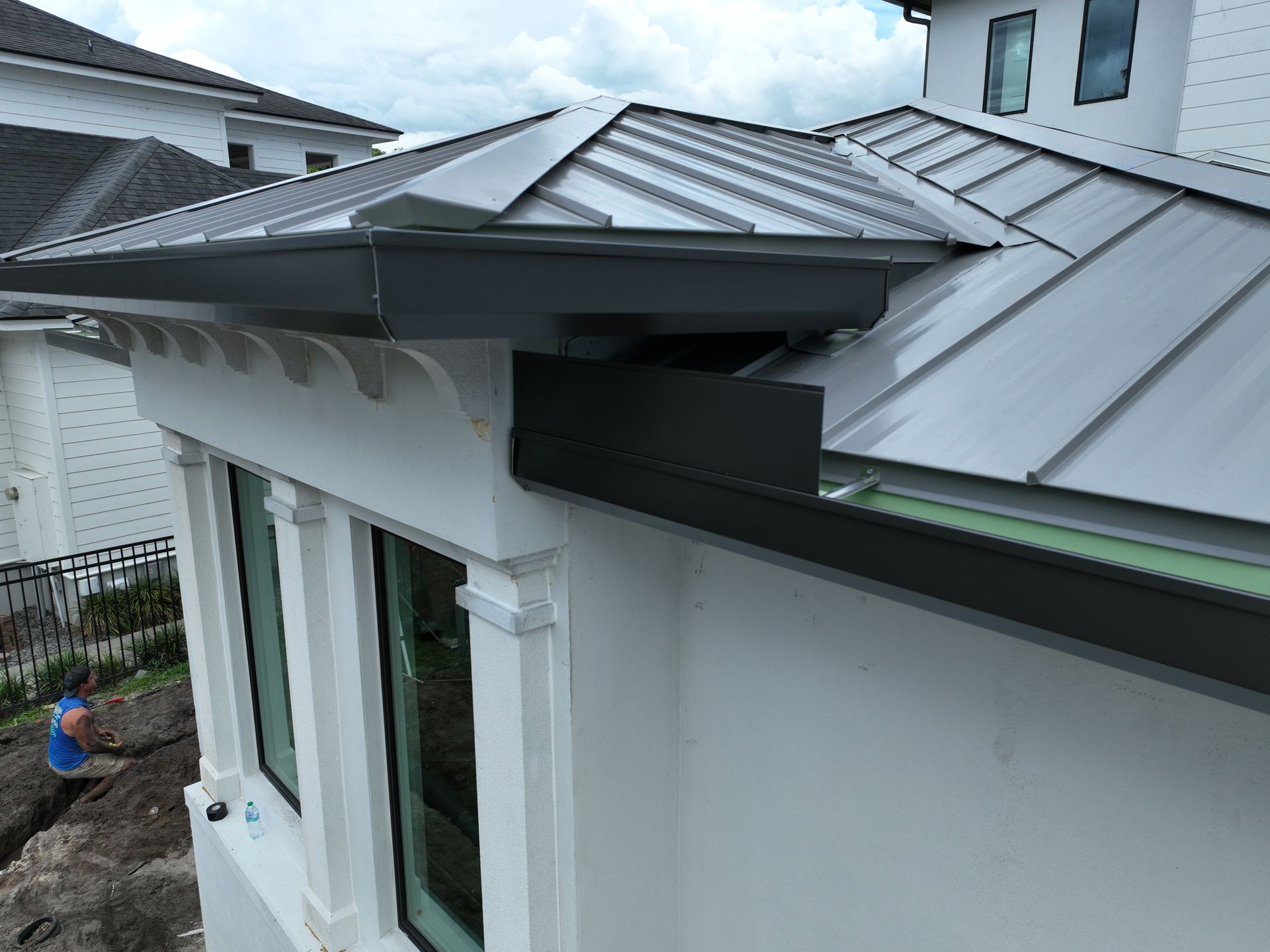 Metal roof edge and gutter on a white house, with a worker crouched below on the left