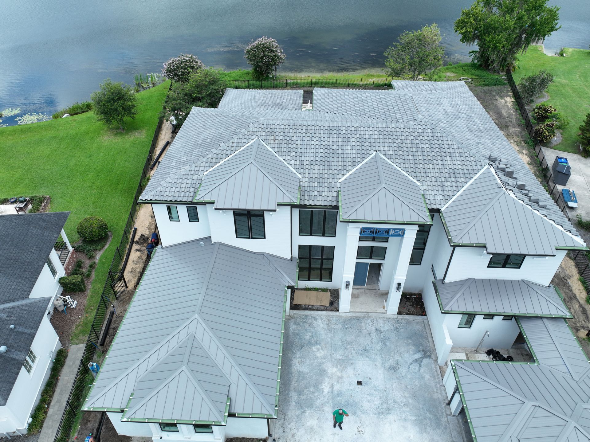 Aerial view of a large white house with gray roof and driveway beside a lake and green lawn