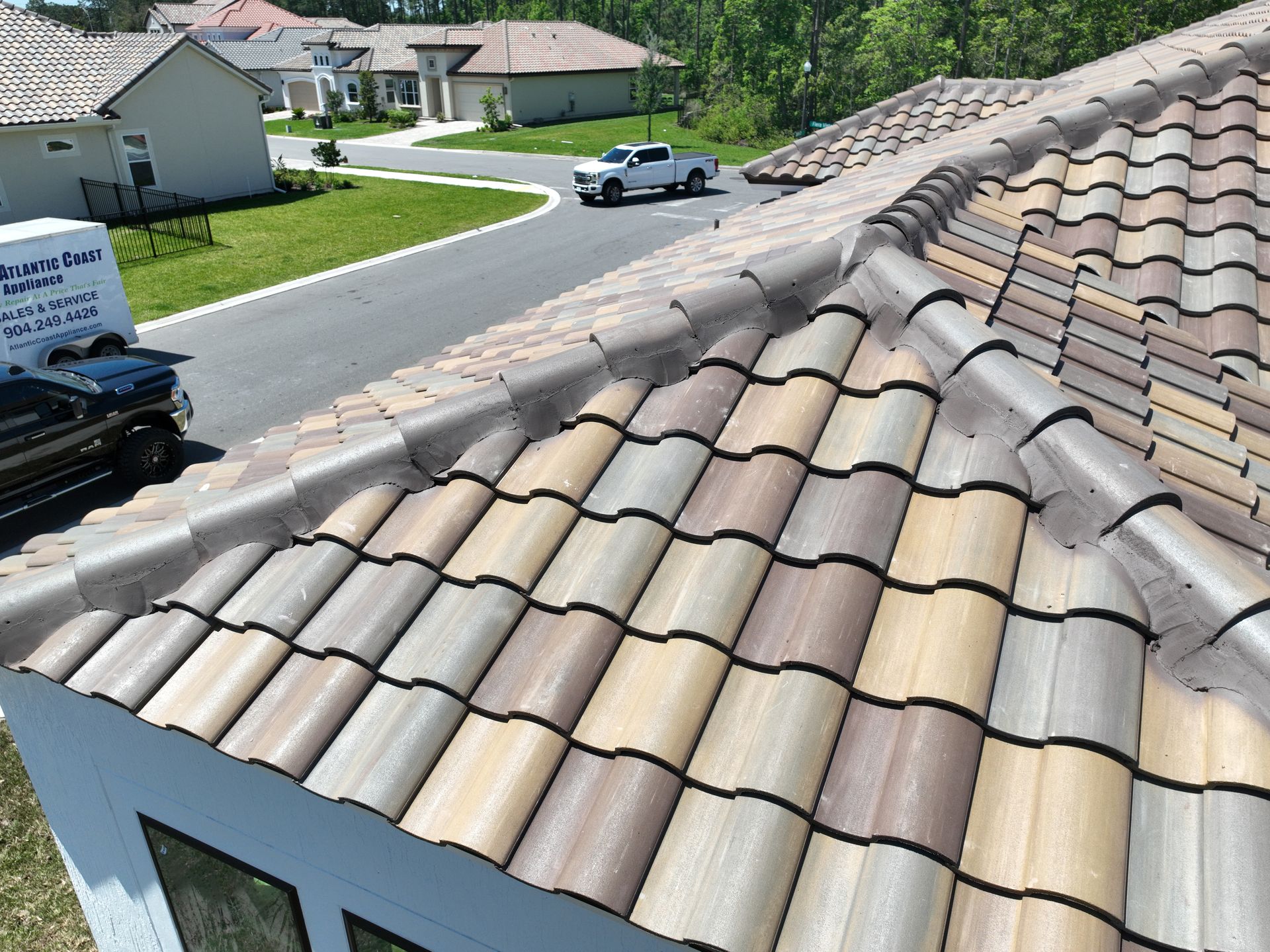 Rooftop view of tan tiled houses and a quiet suburban street with a parked car and green lawns