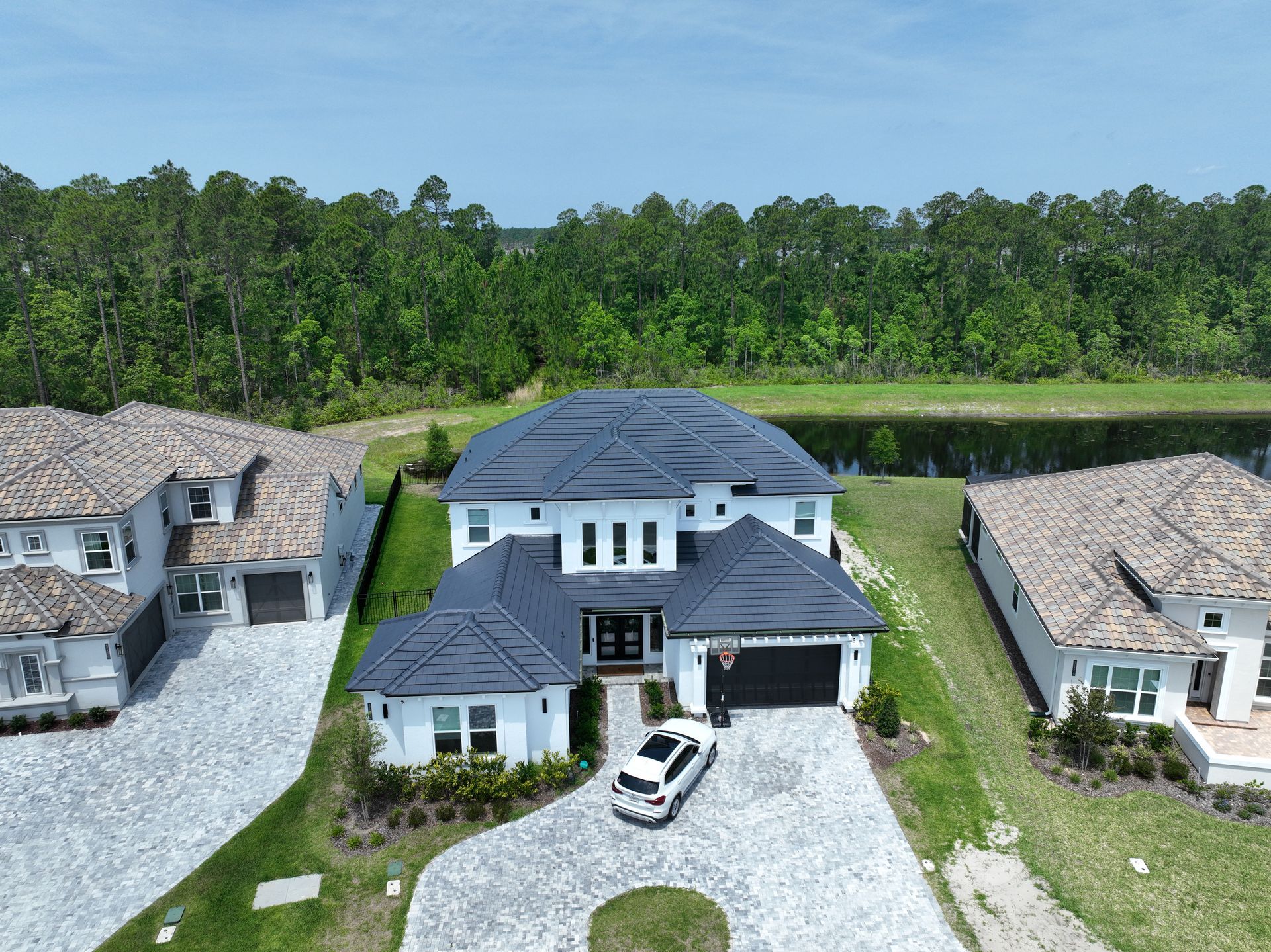 Aerial view of a modern two-story house with a white car in the driveway, surrounded by trees and neighboring homes