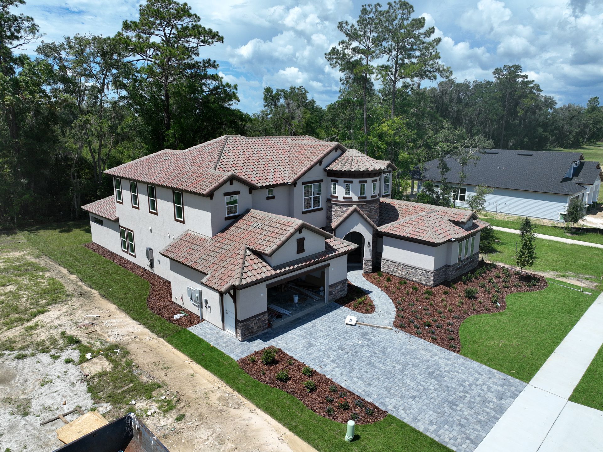 Aerial view of a large modern two-story house with a tiled roof, driveway, and landscaped yard.