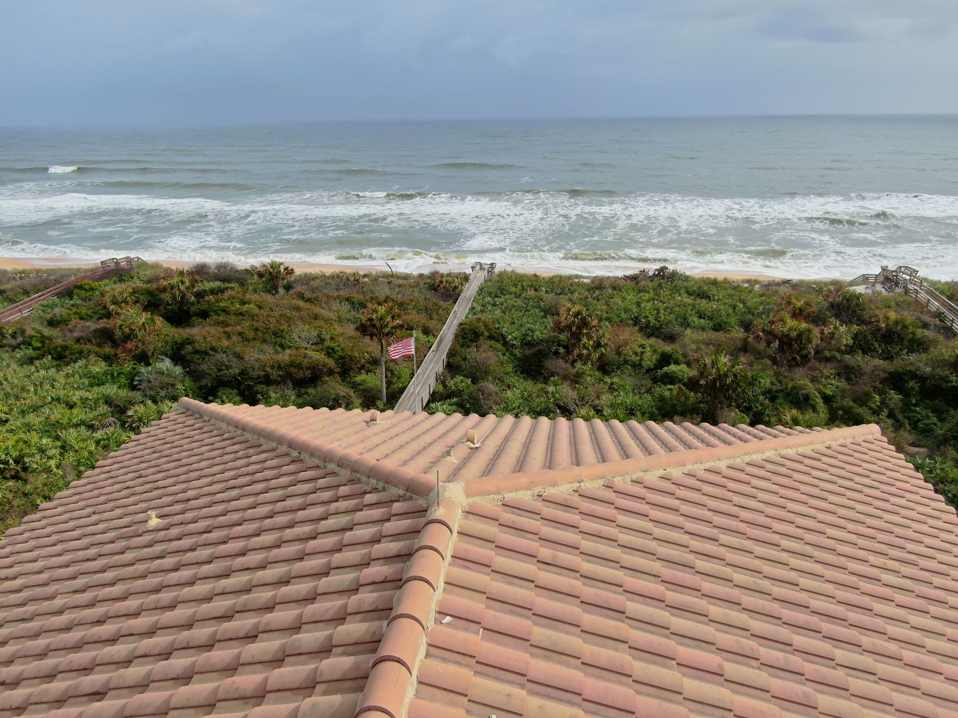 Tiled rooftop overlooking a grassy dune and ocean waves under a cloudy sky