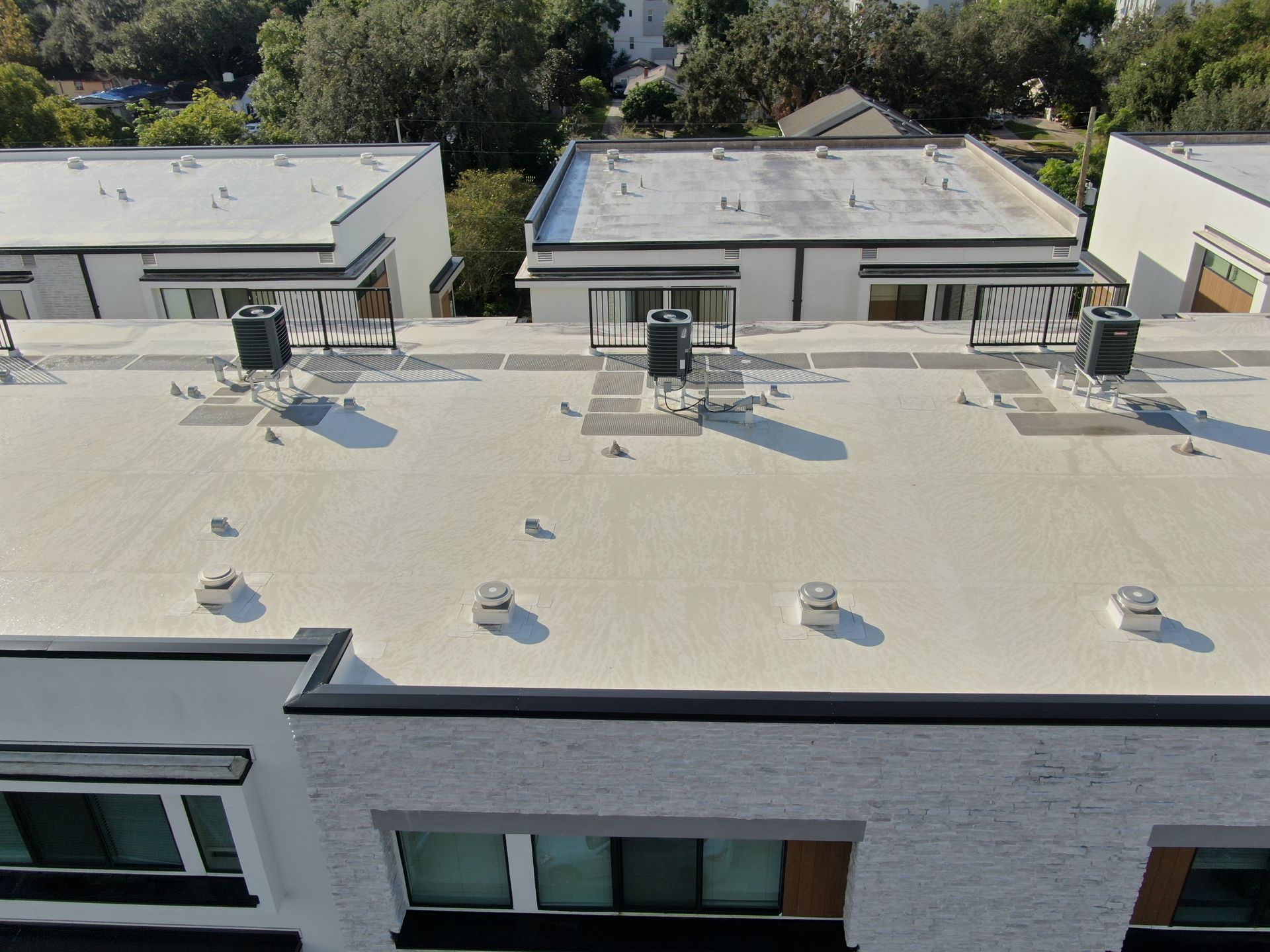 Rooftop with several HVAC units and vents on a flat white commercial building roof.