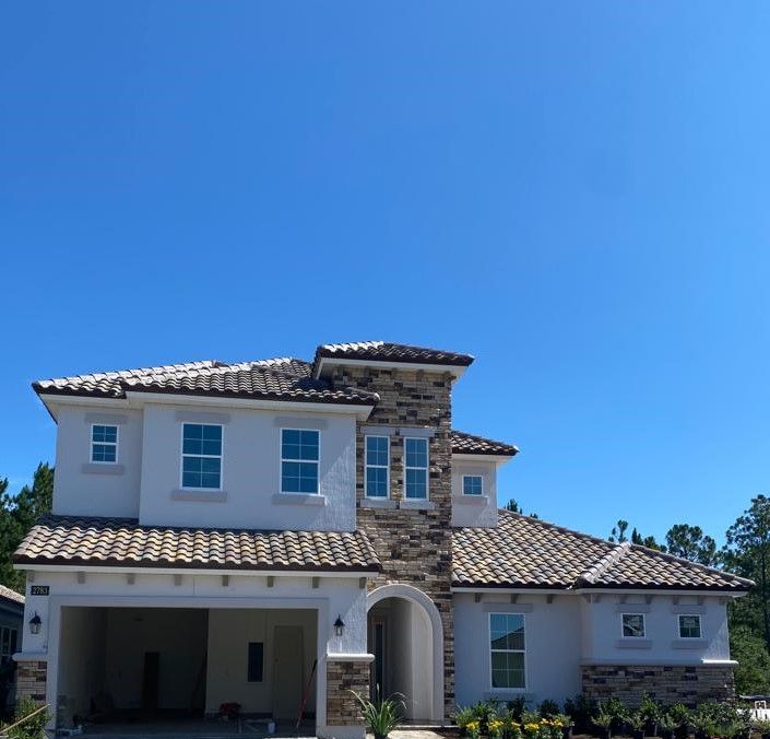 Two-story suburban house with a tiled roof, stone entry, and clear blue sky.