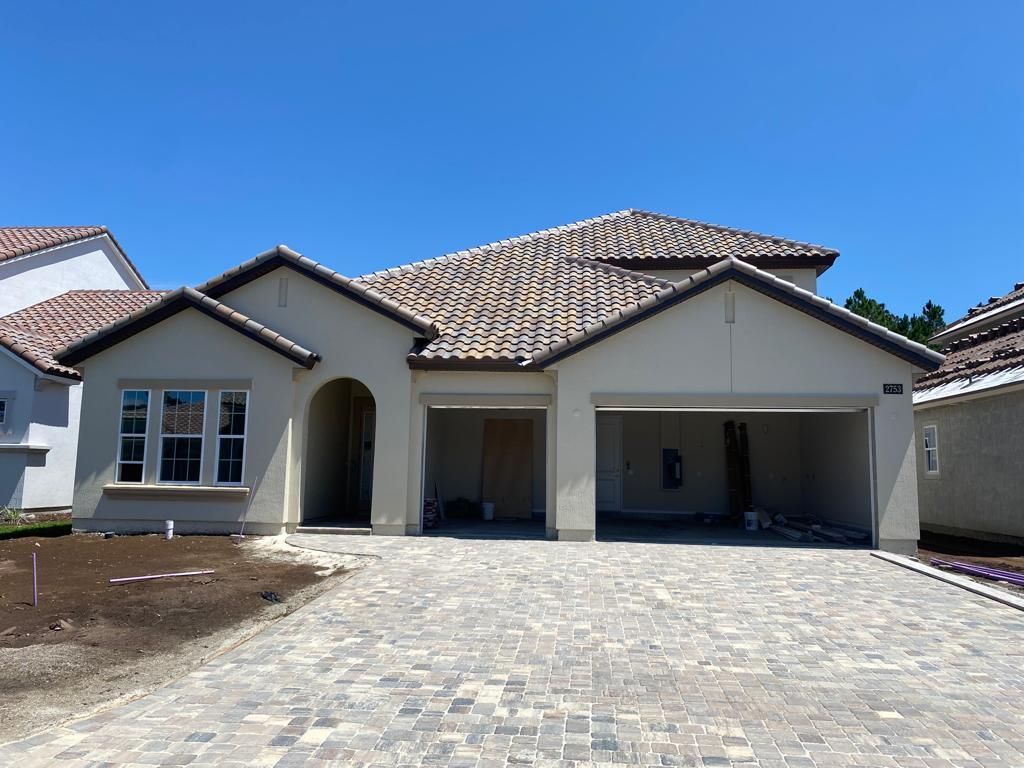Newly built suburban house with stone driveway, tiled roof, and double garage under clear blue sky