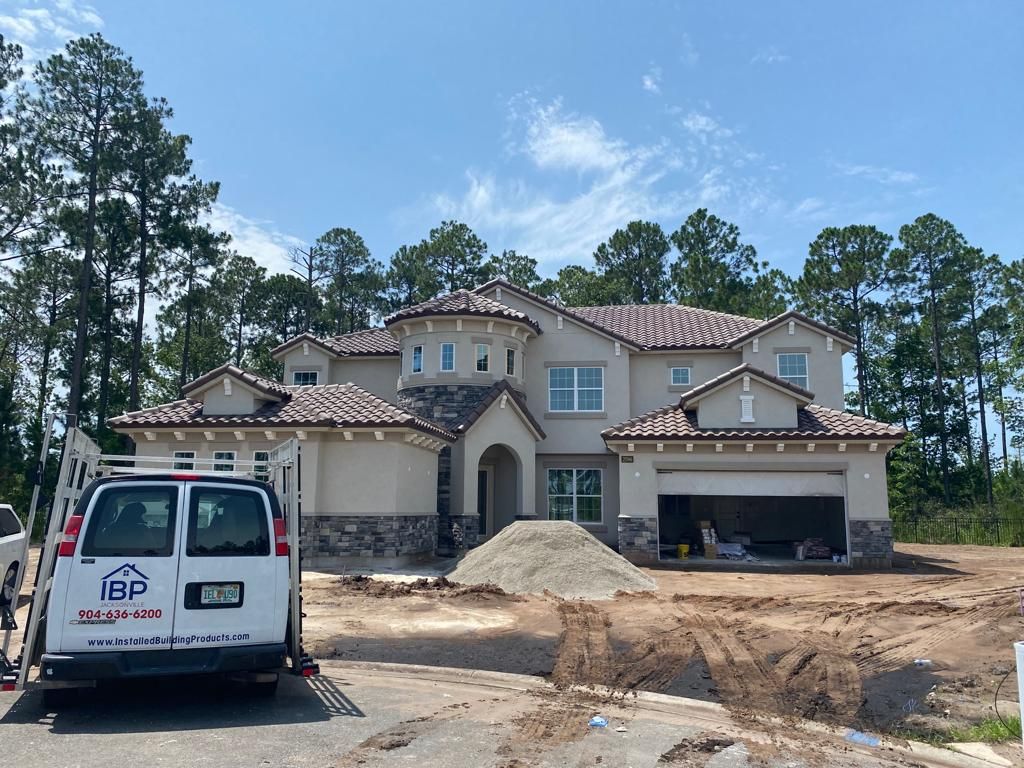 New house under construction with a white van, dirt driveway, and tall pine trees nearby