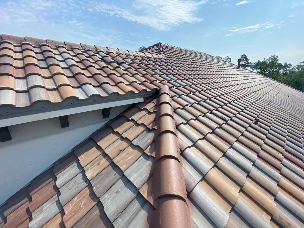 Close-up of a tiled roof with weathered terracotta and beige tiles under a blue sky
