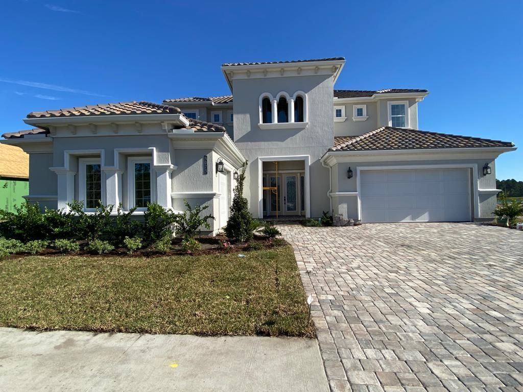 Large modern white stucco house with a tiled roof and paved driveway under a blue sky