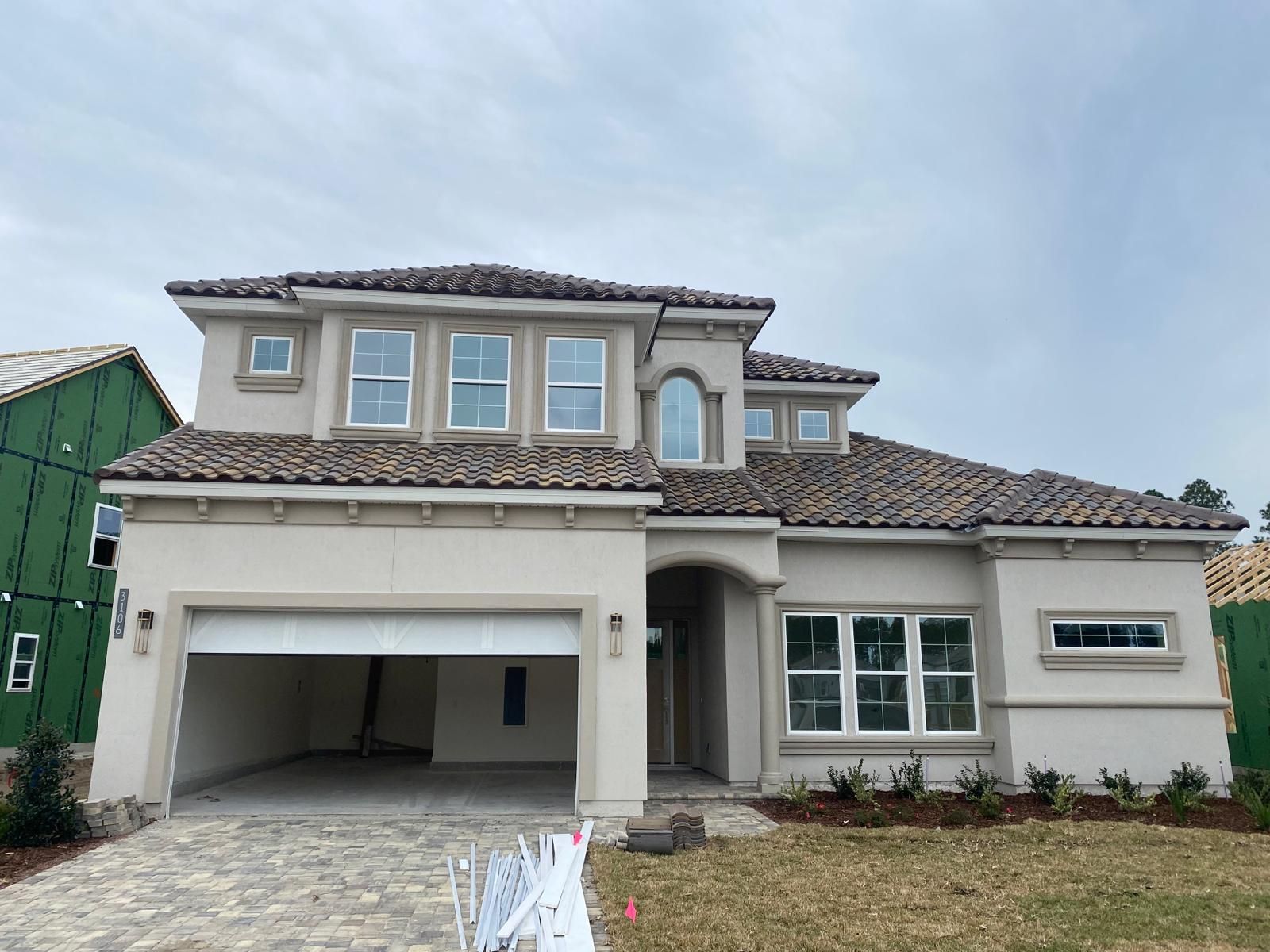 New two-story beige house with a tiled roof, garage, and front lawn under a blue sky