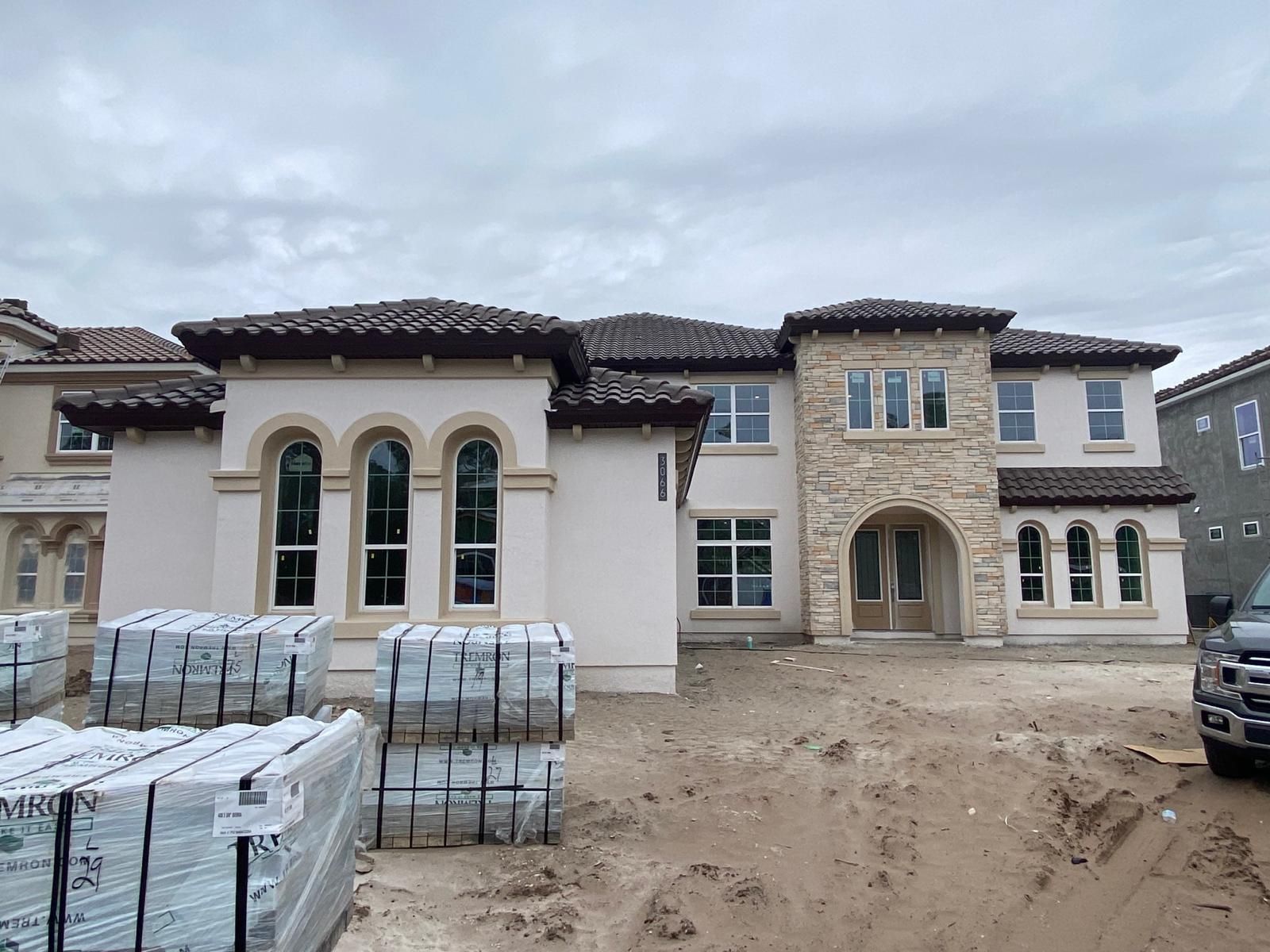New luxury homes under construction with stacked building materials and a dirt driveway.