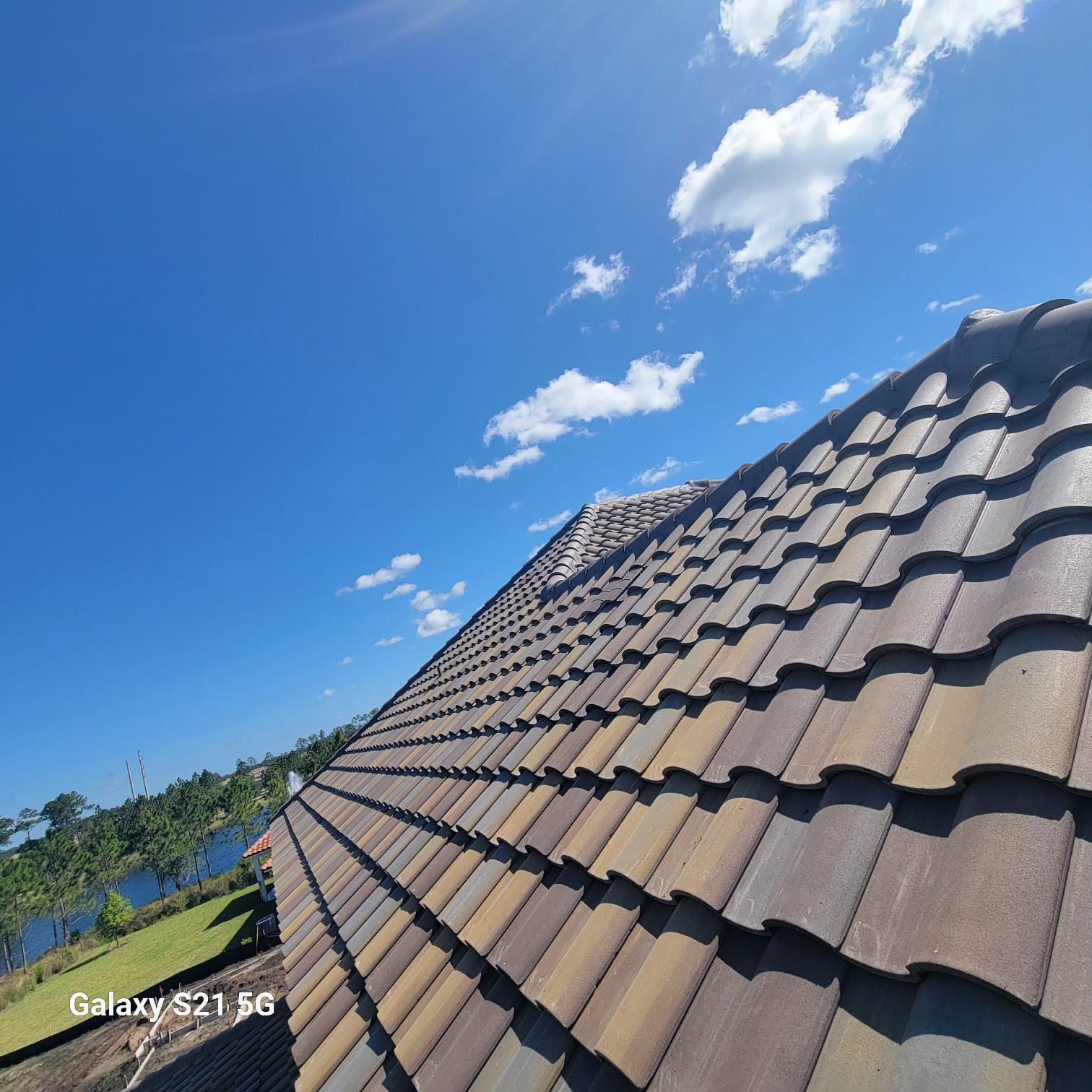 Low-angle view of a red-tiled roof against a bright blue sky with scattered clouds