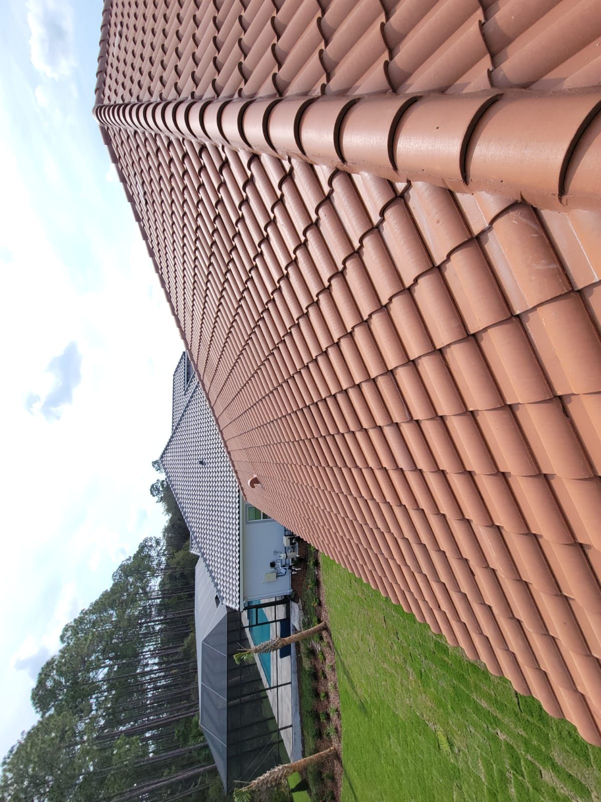 Tilted view of a house with terracotta roof tiles, green lawn, and cloudy sky in the background