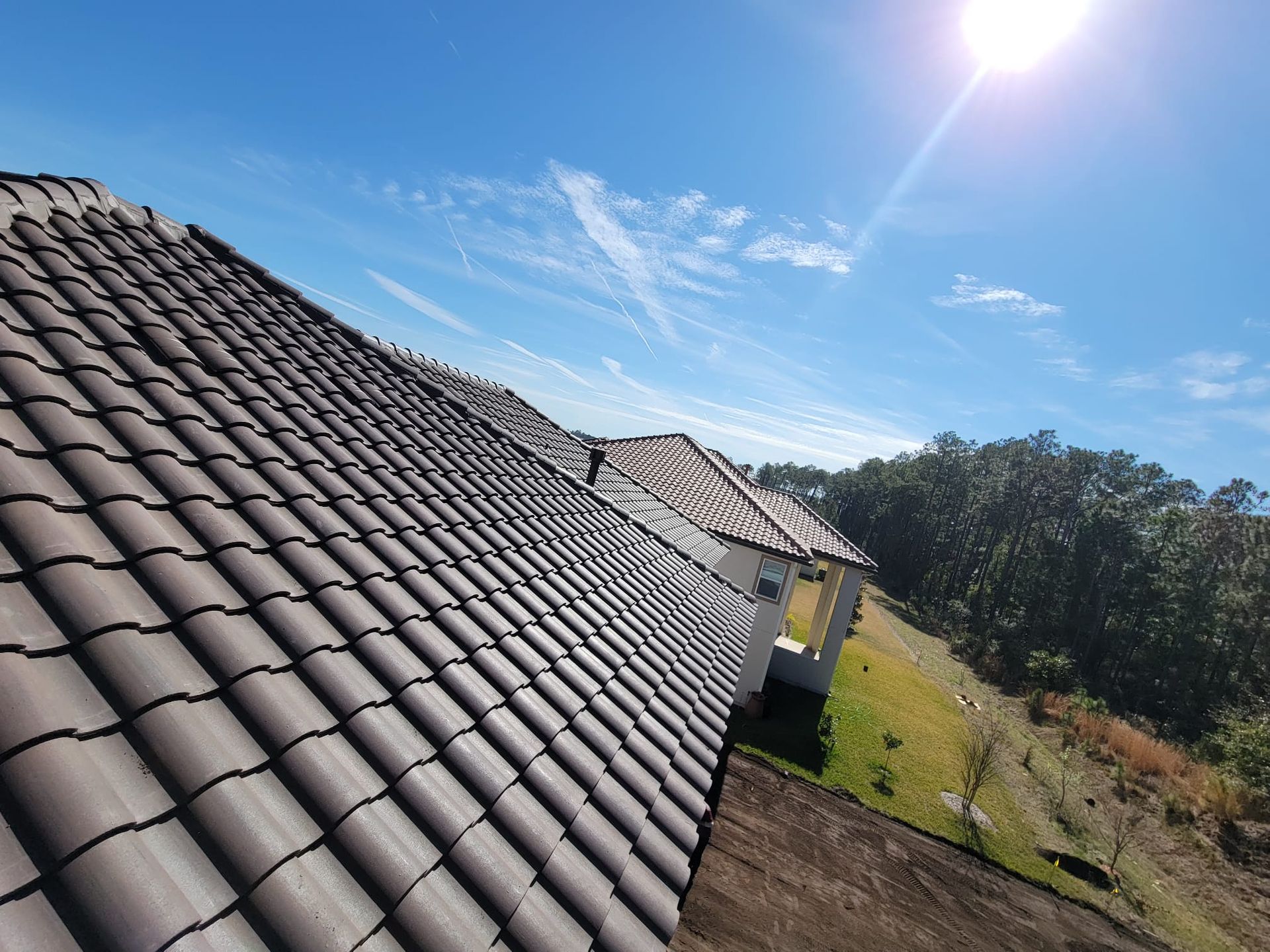 Sunlit tiled roof beside grassy yard and trees under a clear blue sky