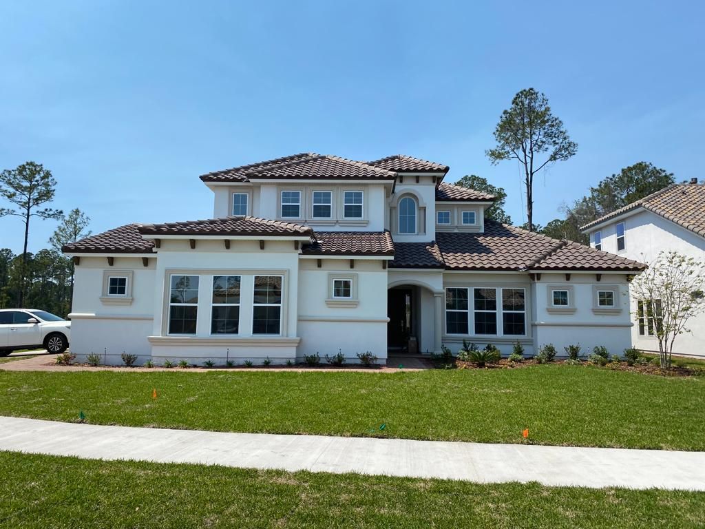 Large two-story white stucco house with a red tile roof and manicured lawn under a clear blue sky