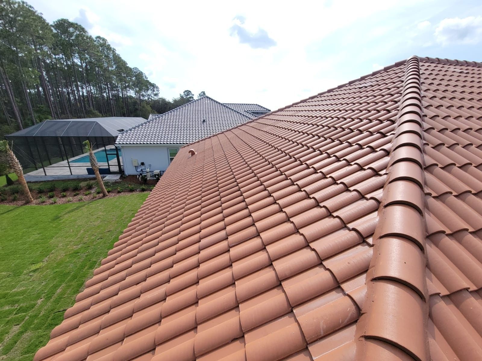 Terracotta tiled roof beside a grassy yard and houses under a cloudy sky