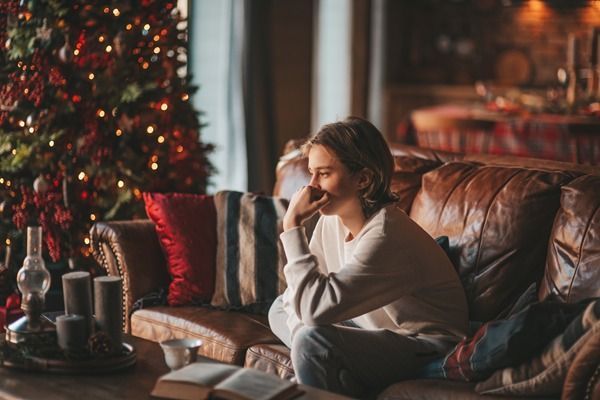 Person sitting on a leather couch beside a lit Christmas tree in a cozy living room