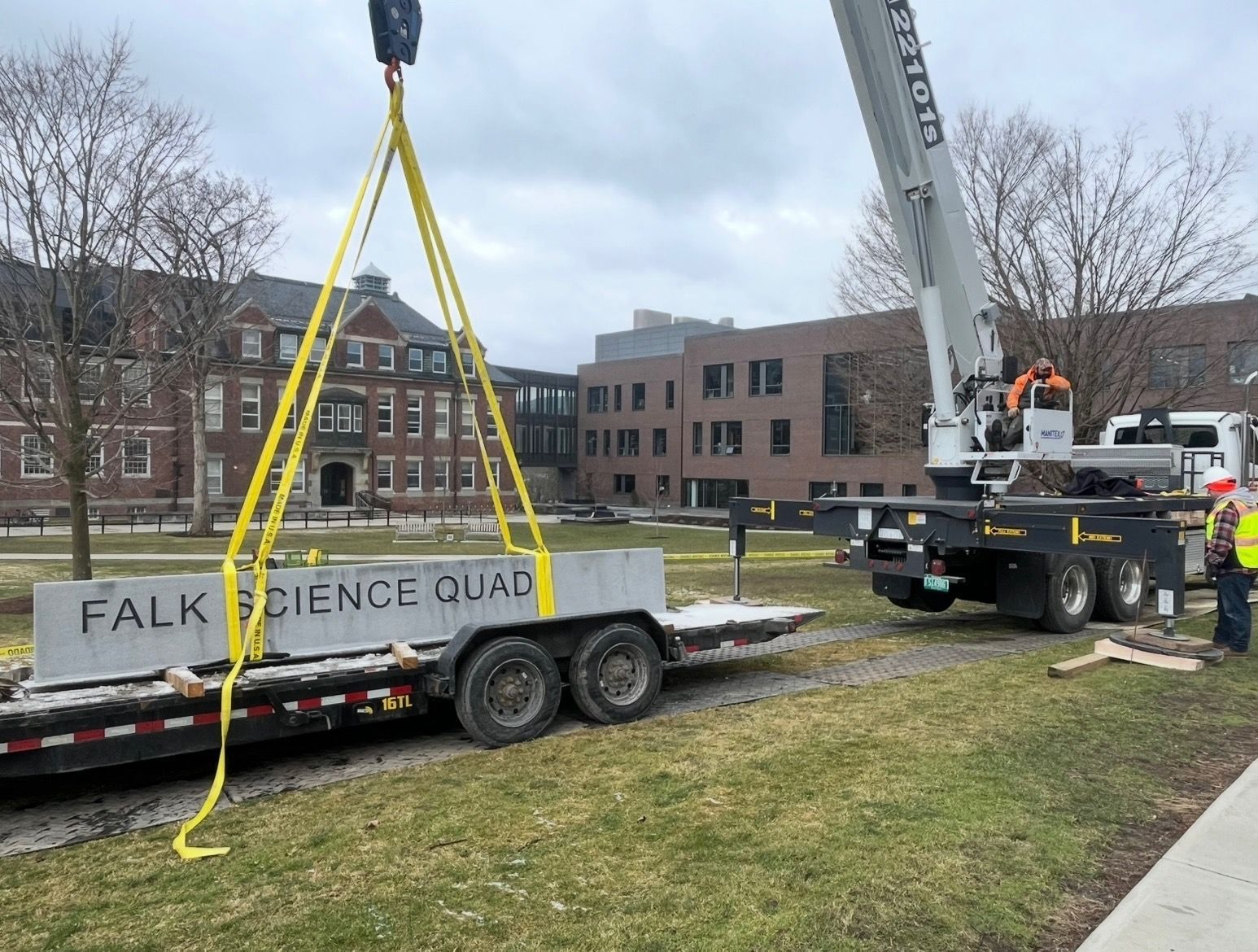 A crane hoists a stone monument labeled 