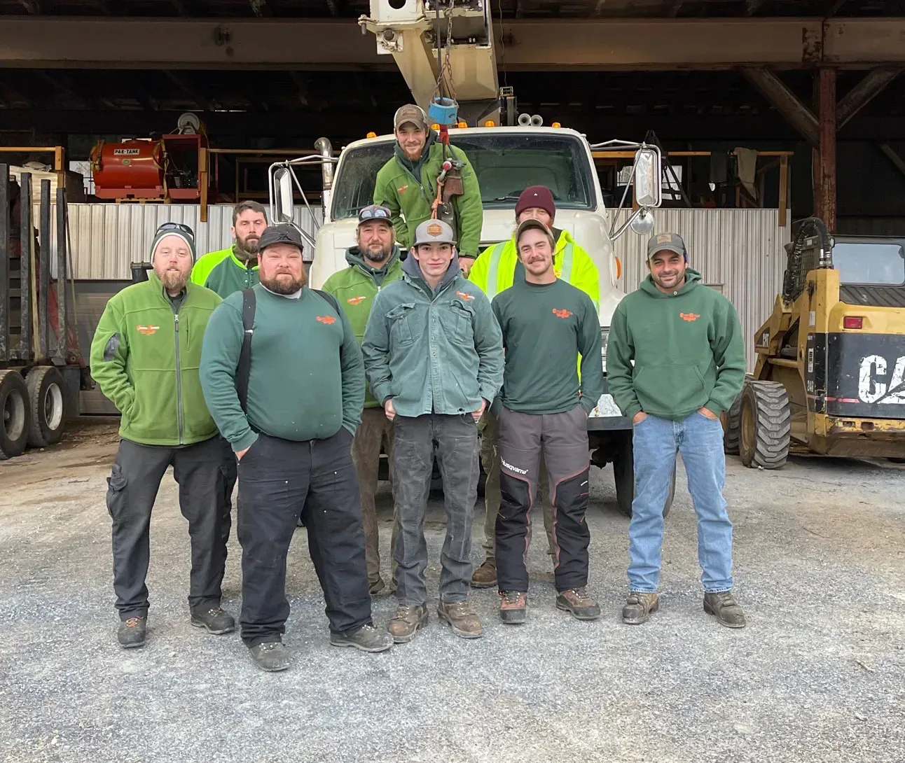 Group of workers in green jackets, standing in front of a white truck and machinery.