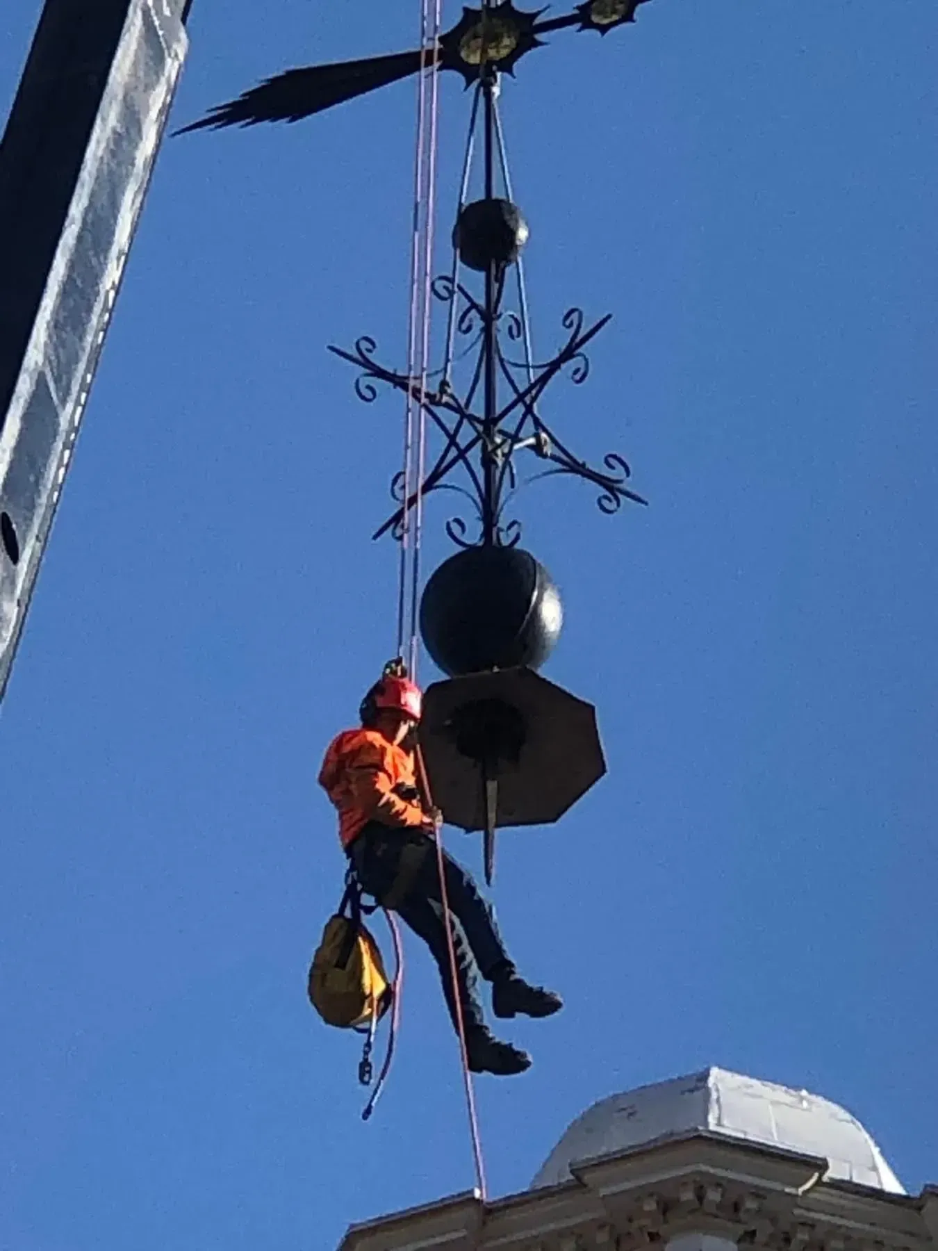 Worker suspended by ropes near a decorative street lamp against a blue sky.