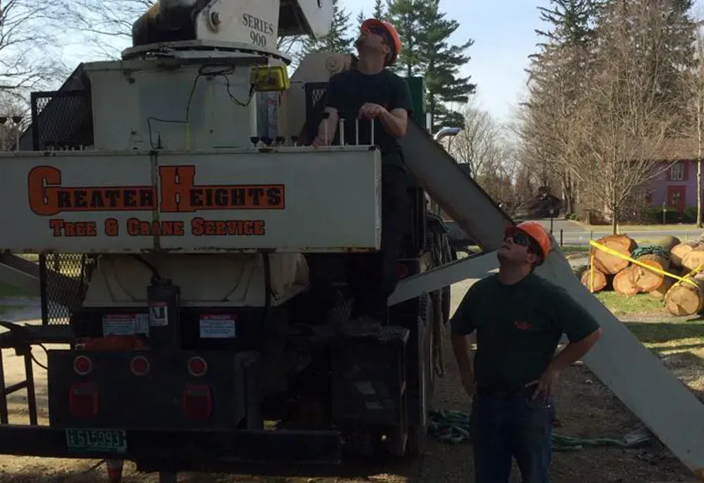 Two workers in safety gear inspect a tree chipper in front of a house, outdoors.