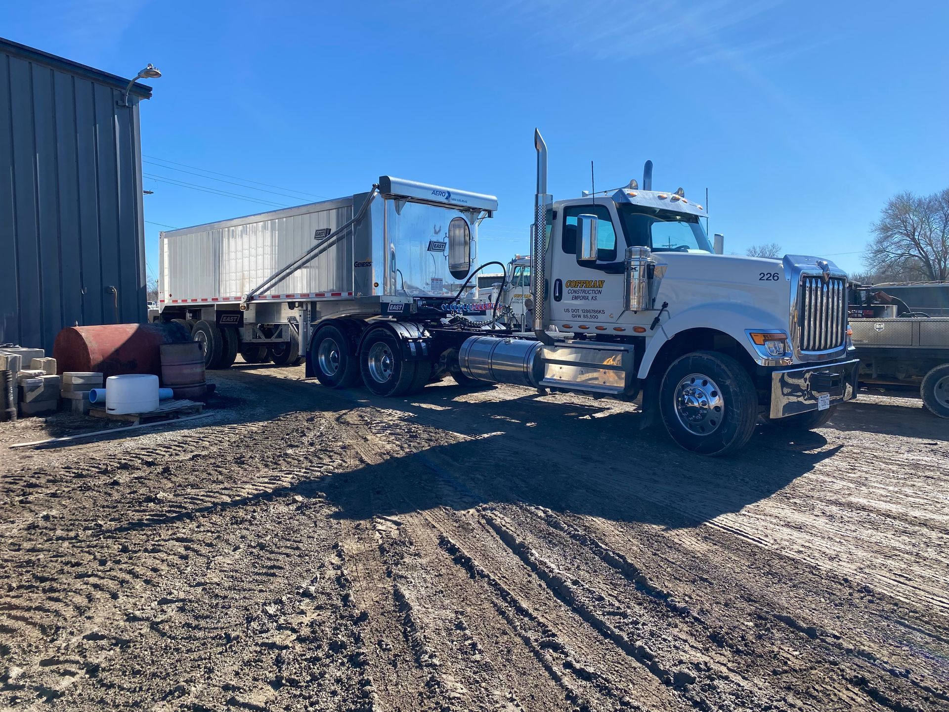 a white semi truck is parked in a dirt lot next to a building