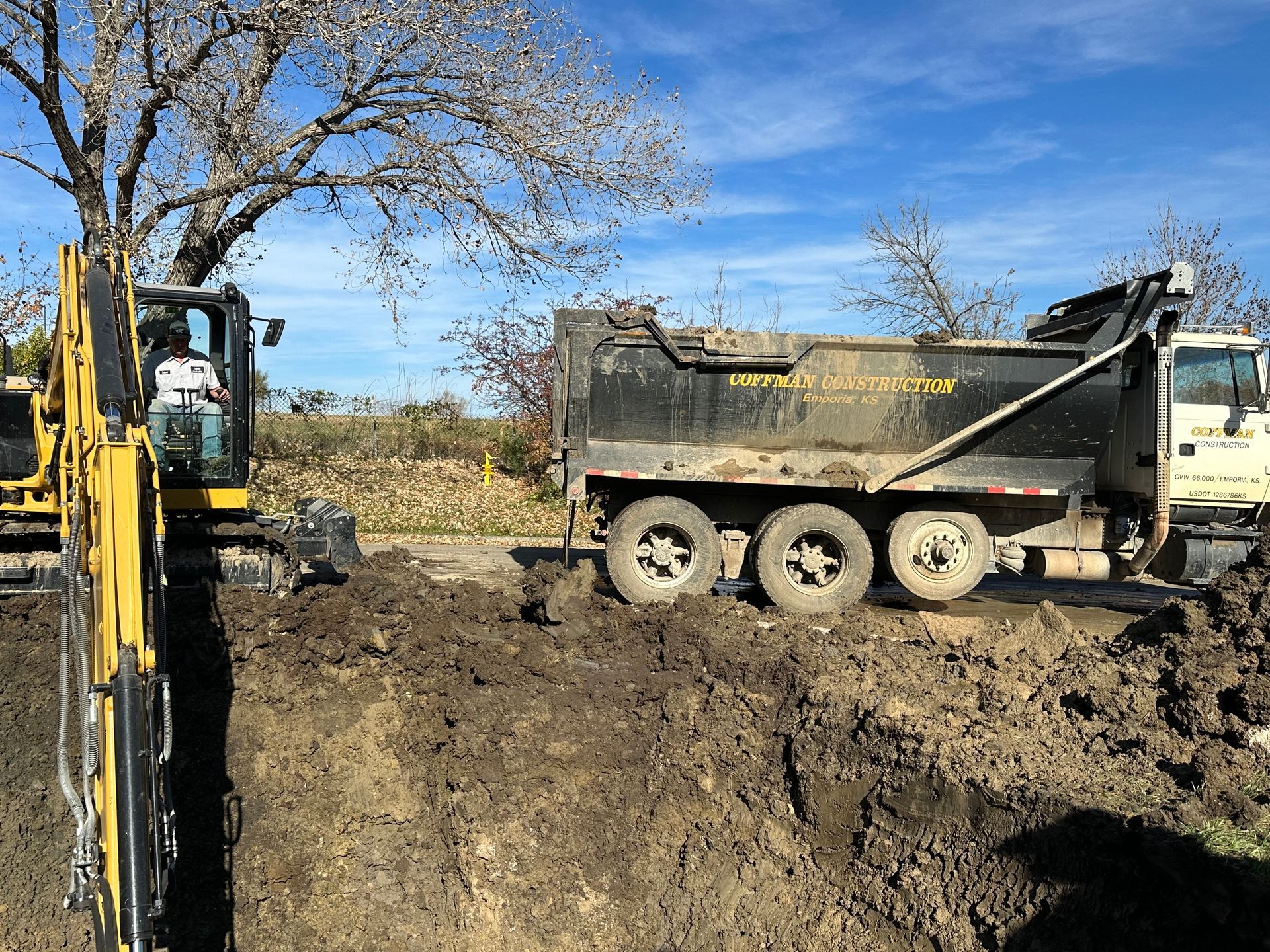 a dump truck is driving through a dirt field next to an excavator