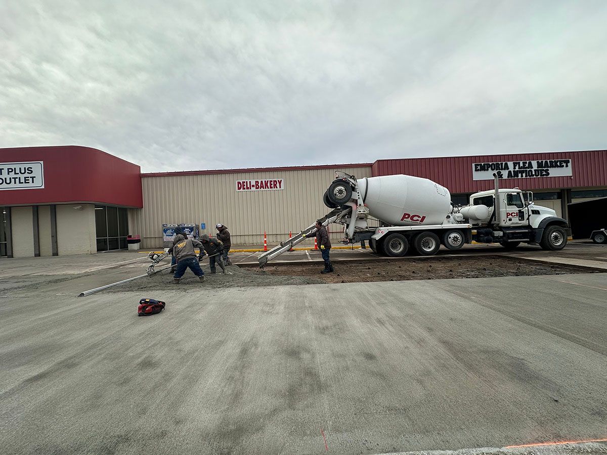 A white concrete mixer truck and the crew from SR Coffman Construction Inc. laying concrete outside a commercial building