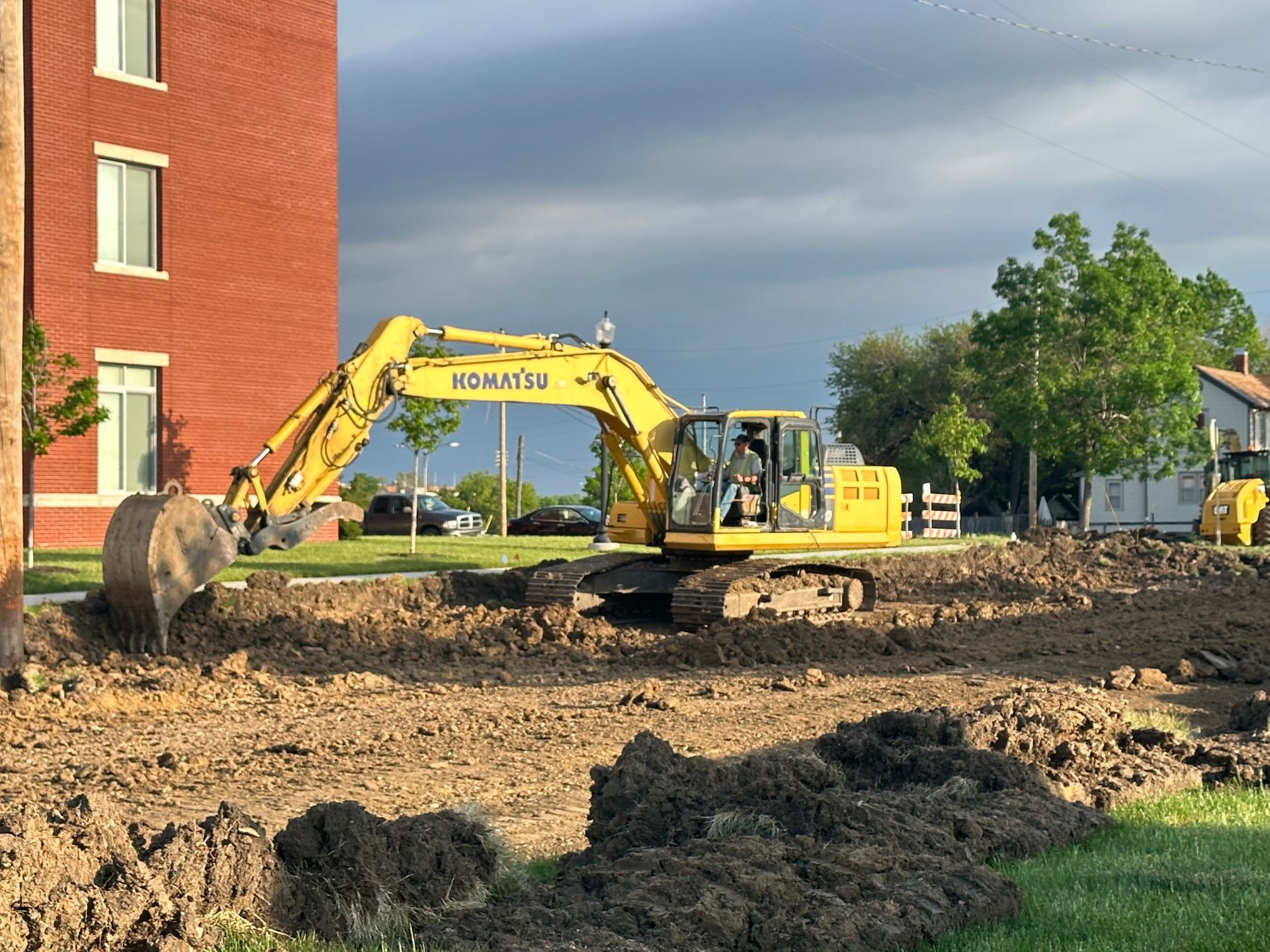 a yellow excavator is digging a hole in the dirt in front of a brick building