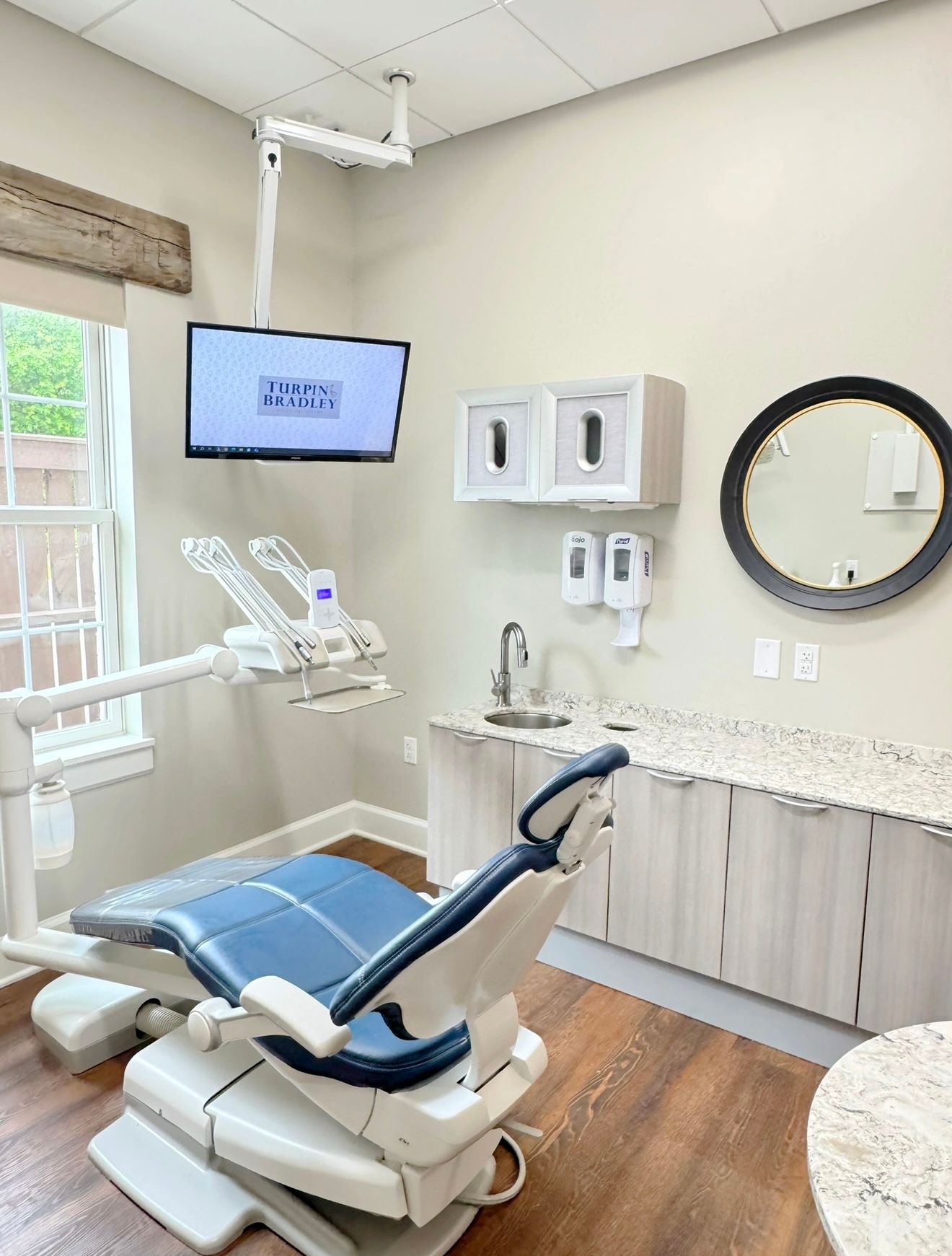A dental office with a dental chair , sink , television and mirror.