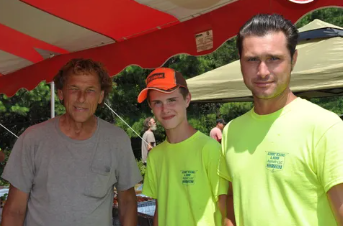A man in a grey shirt is standing next to two men in neon yellow shirts