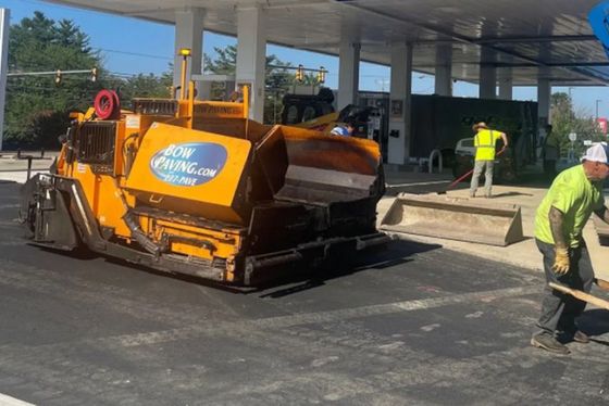 A man is standing in front of a yellow asphalt paving machine.