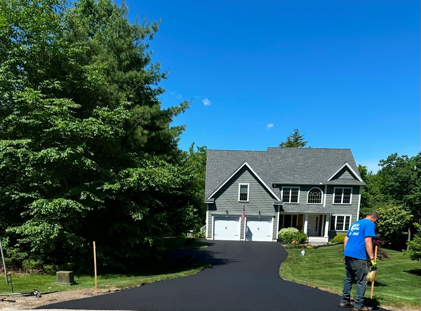 A man in a blue shirt is paving a driveway in front of a large house.
