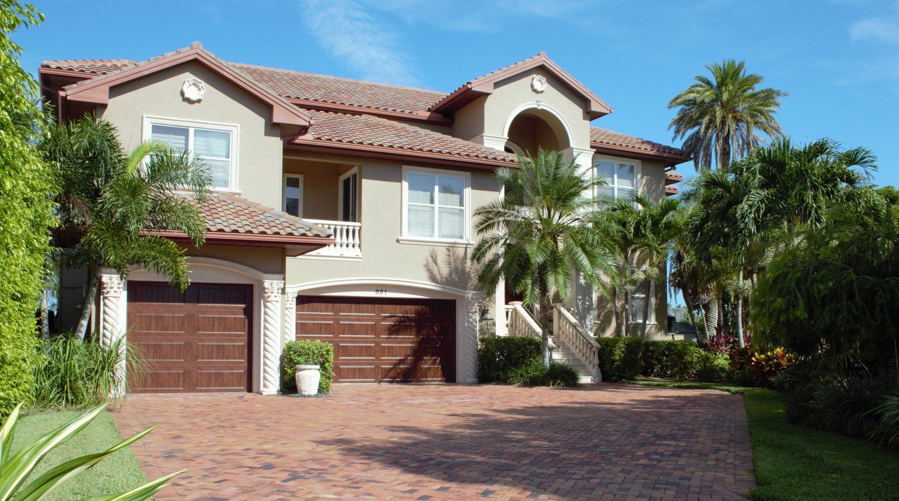 A large house with two garages and palm trees in front of it